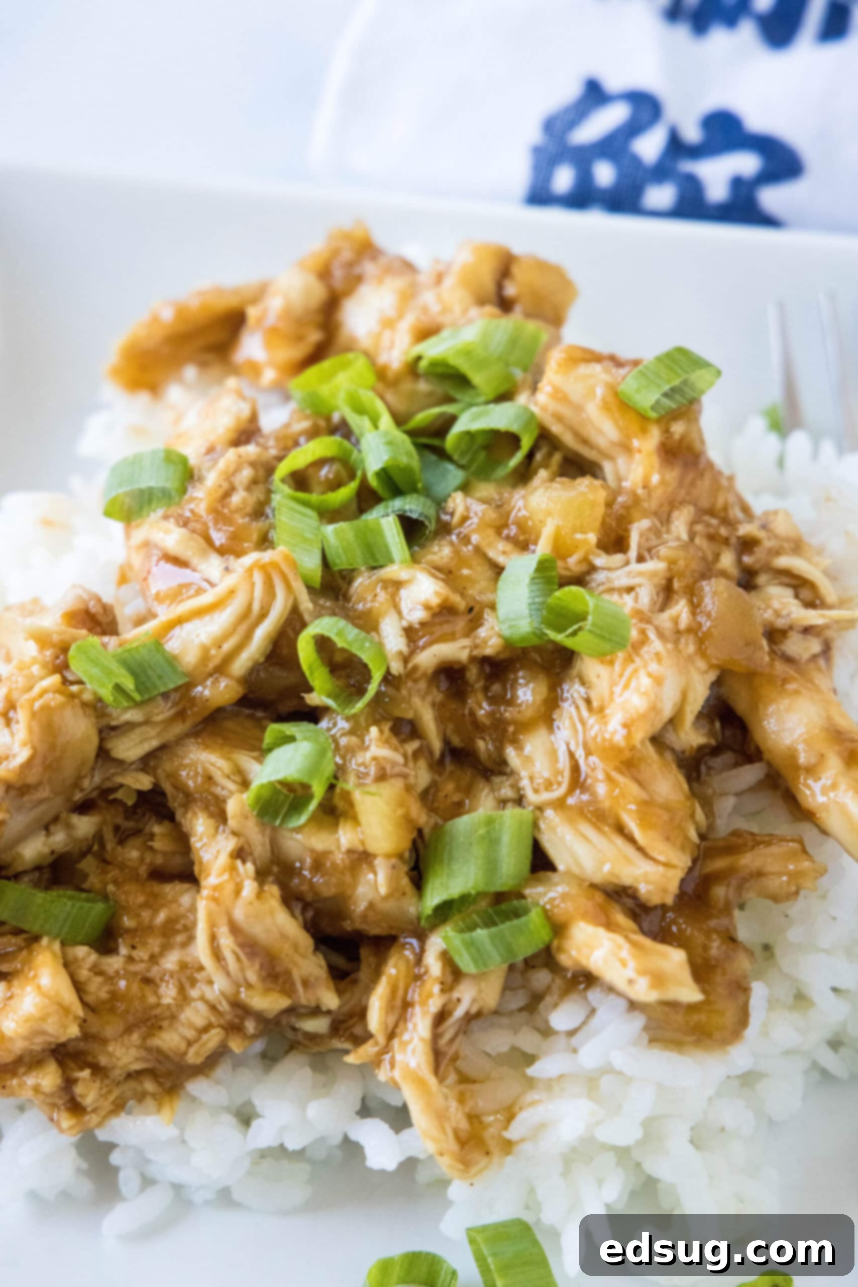 A delicious serving of slow cooker Hawaiian chicken arranged neatly over a bowl of fluffy white rice, garnished with green onions.