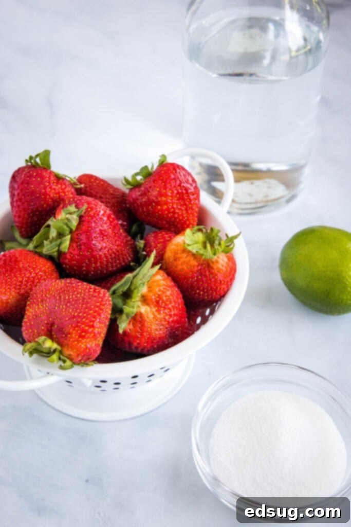 A flat lay image showcasing the fresh ingredients needed for strawberry agua fresca: ripe strawberries, whole limes, granulated sugar, and a pitcher of cold water.