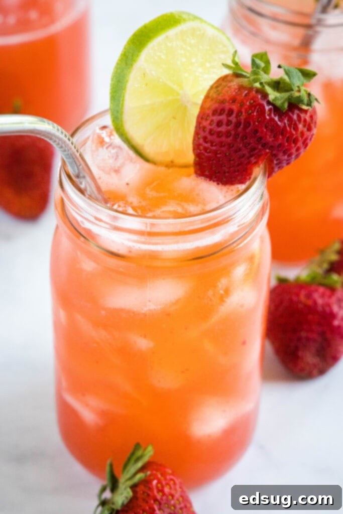 A rustic wooden table displaying a mason jar of strawberry agua fresca with lime, alongside fresh strawberries and limes, evoking a farmhouse aesthetic.