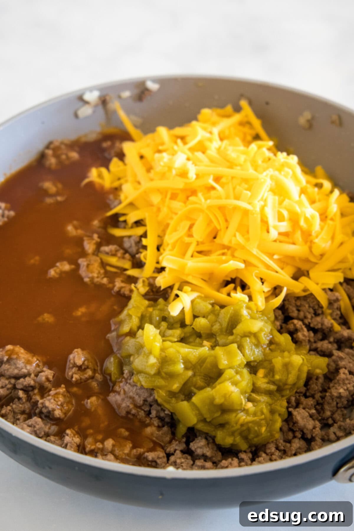 mixing ground beef, enchilada sauce, green chiles and cheddar cheese together