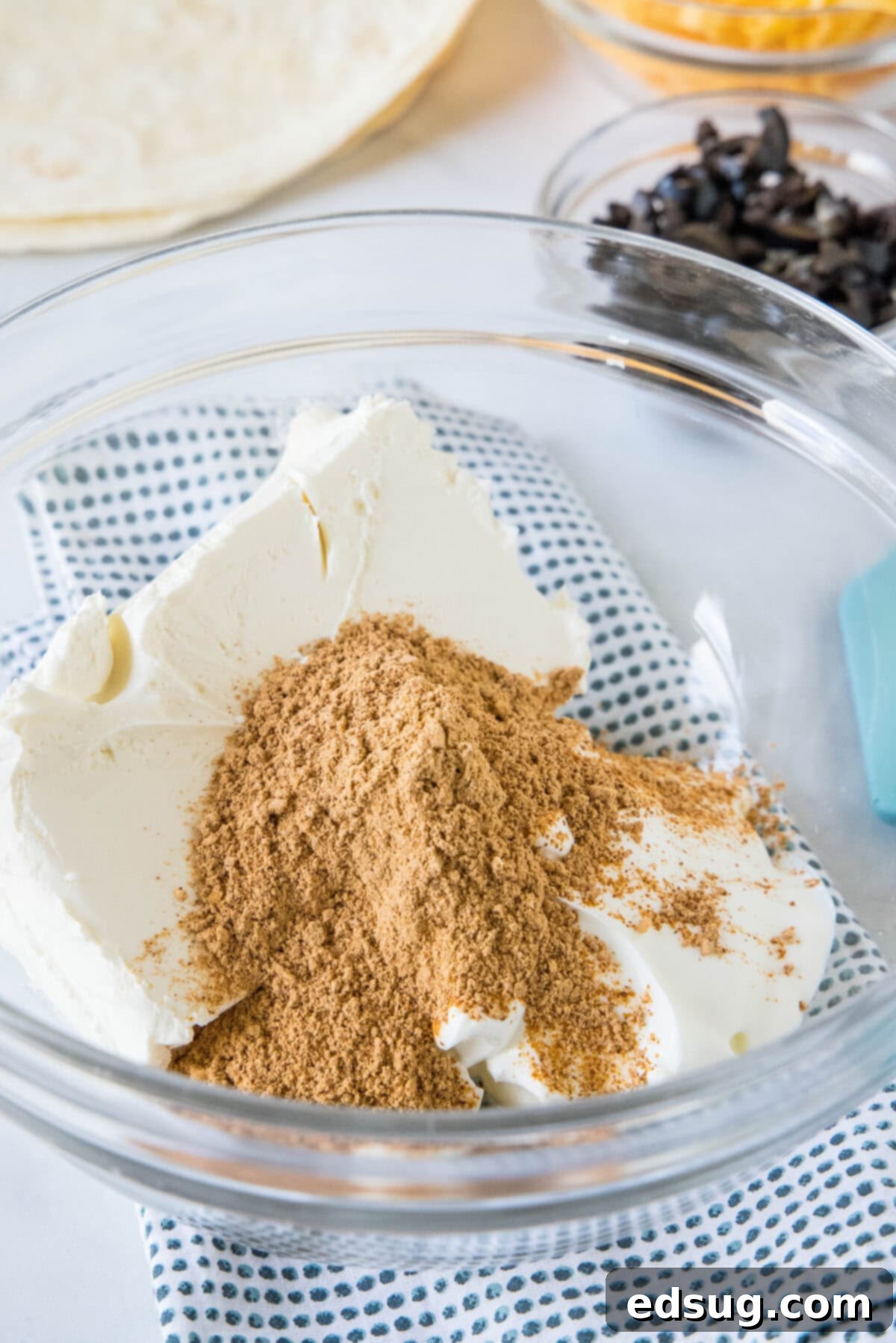 Taco seasoning is added to a glass bowl containing a creamy base of cream cheese and sour cream.
