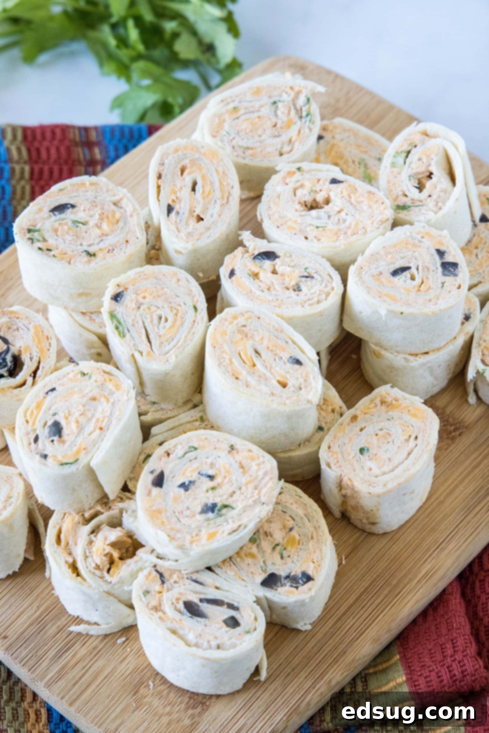 Several neatly sliced taco pinwheels stacked on a rustic wooden cutting board, ready for a party.