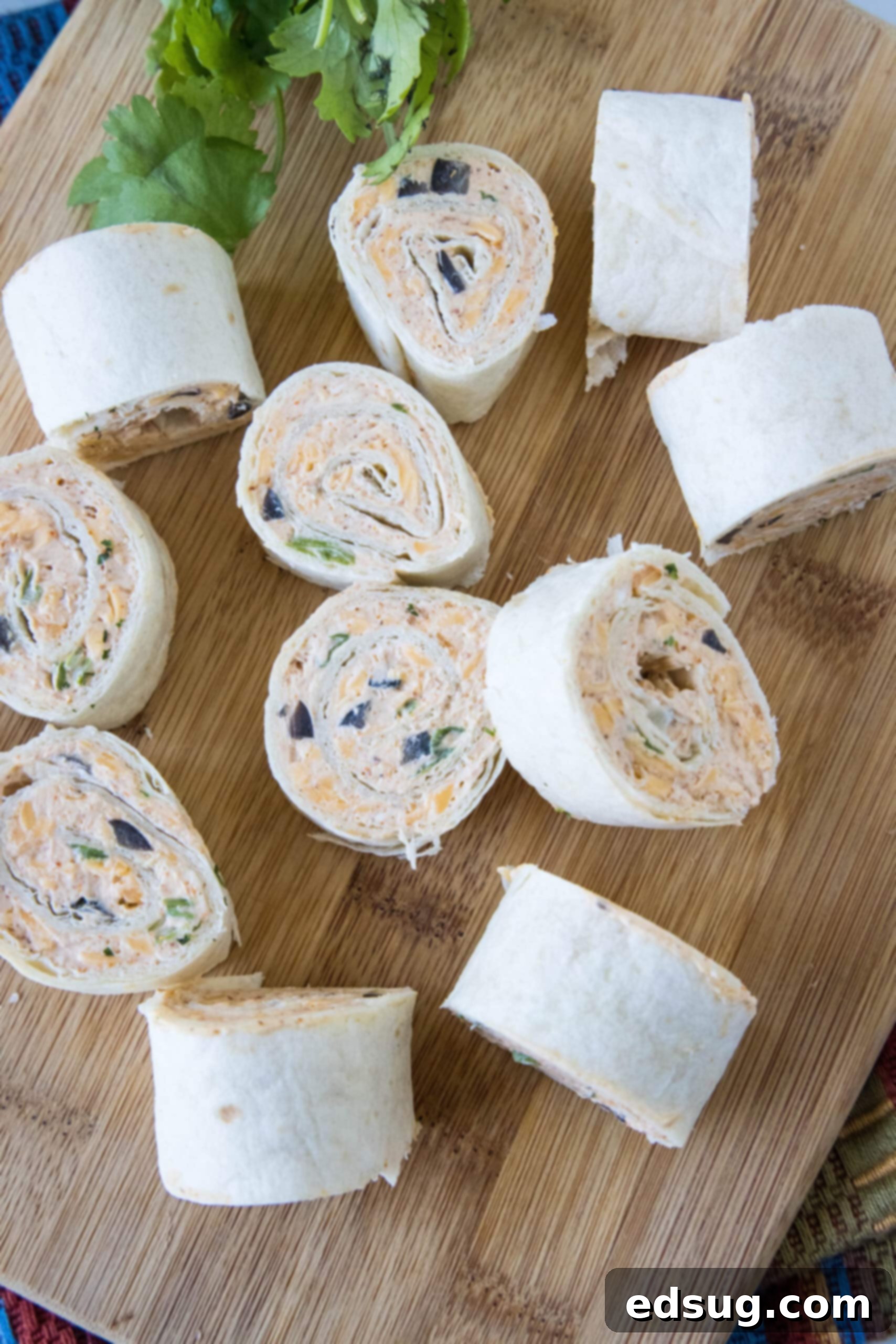 An overhead shot showcasing an assortment of colorful taco pinwheels artfully arranged on a wooden cutting board, with some standing upright and others laid flat.