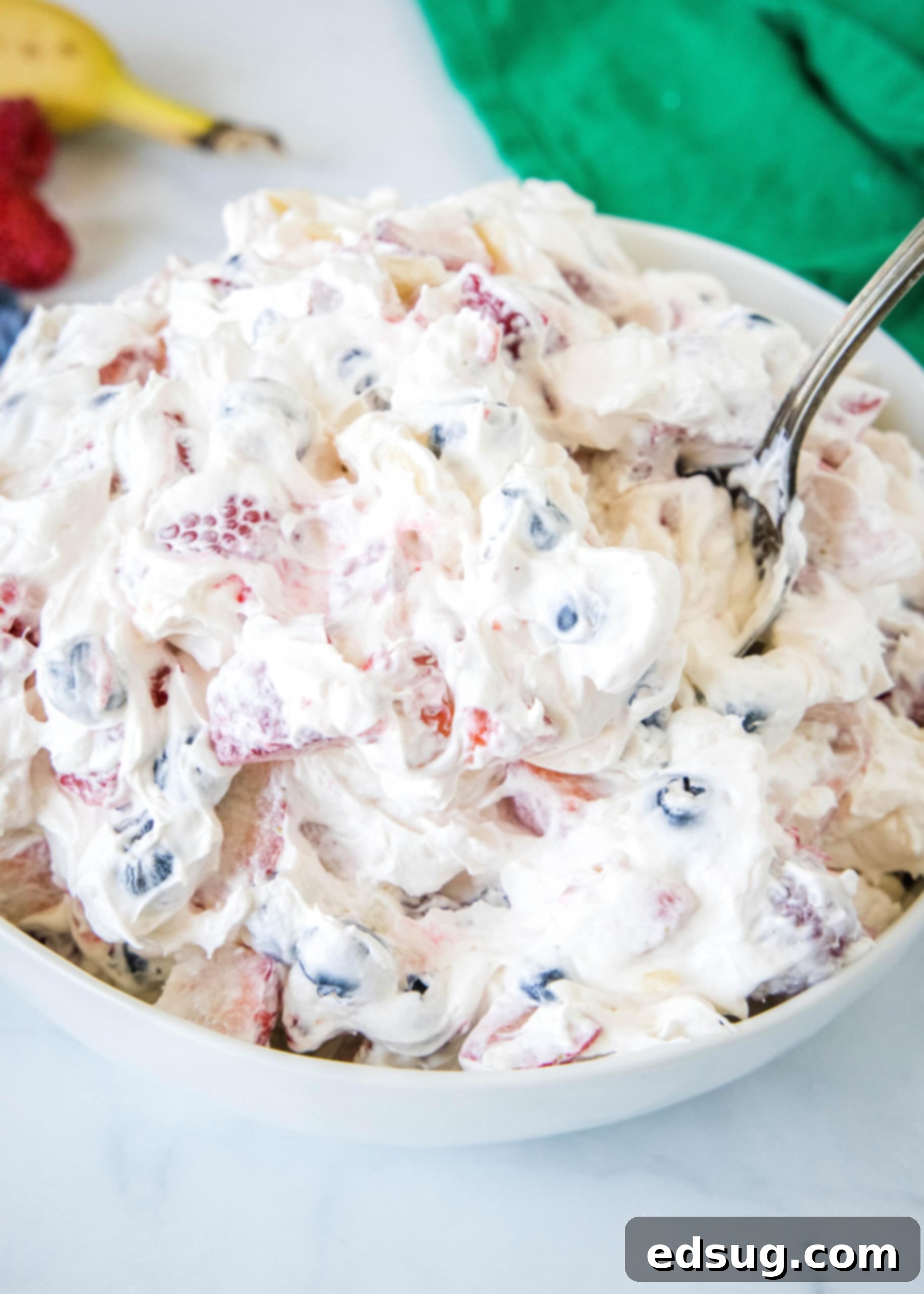 Cheesecake fruit salad in a bowl with a spoon for serving.