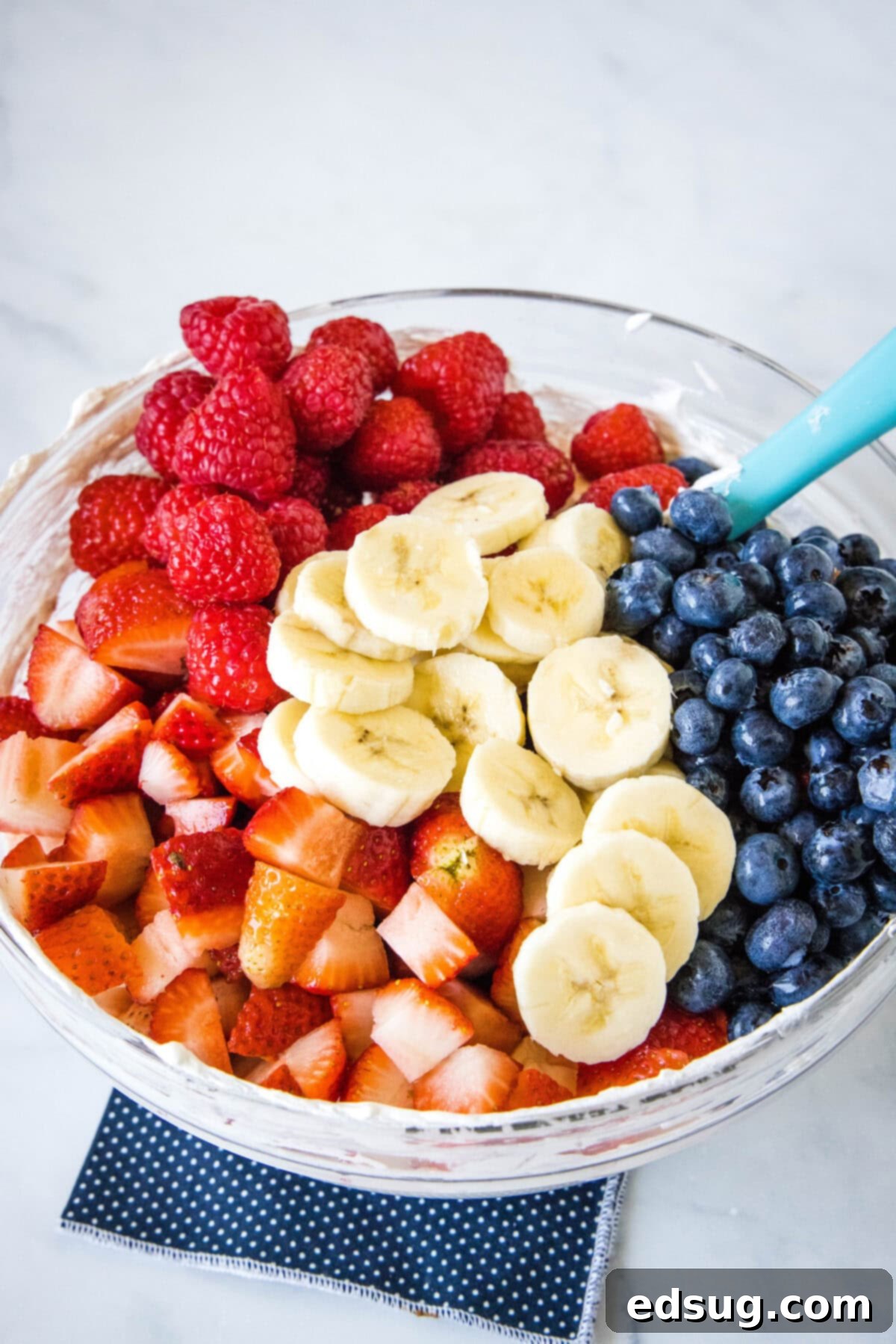 Fresh berries and bananas added to a bowl of whipped cream cheese dressing.