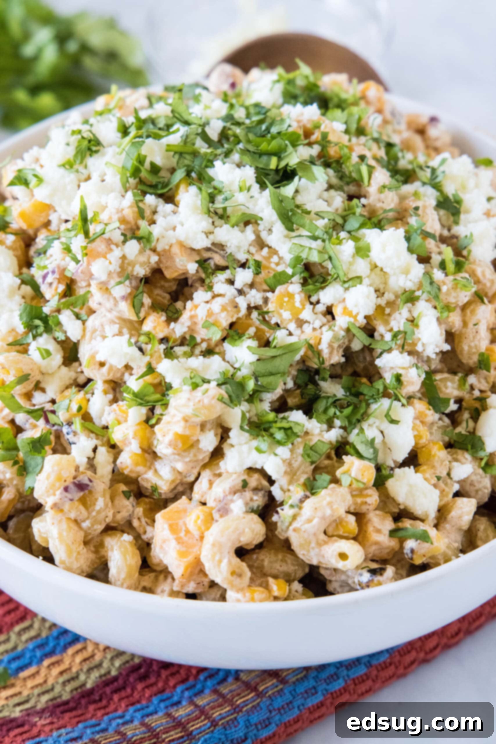 A vibrant bowl of Mexican street corn pasta salad, garnished with crumbled Cotija cheese and fresh cilantro.