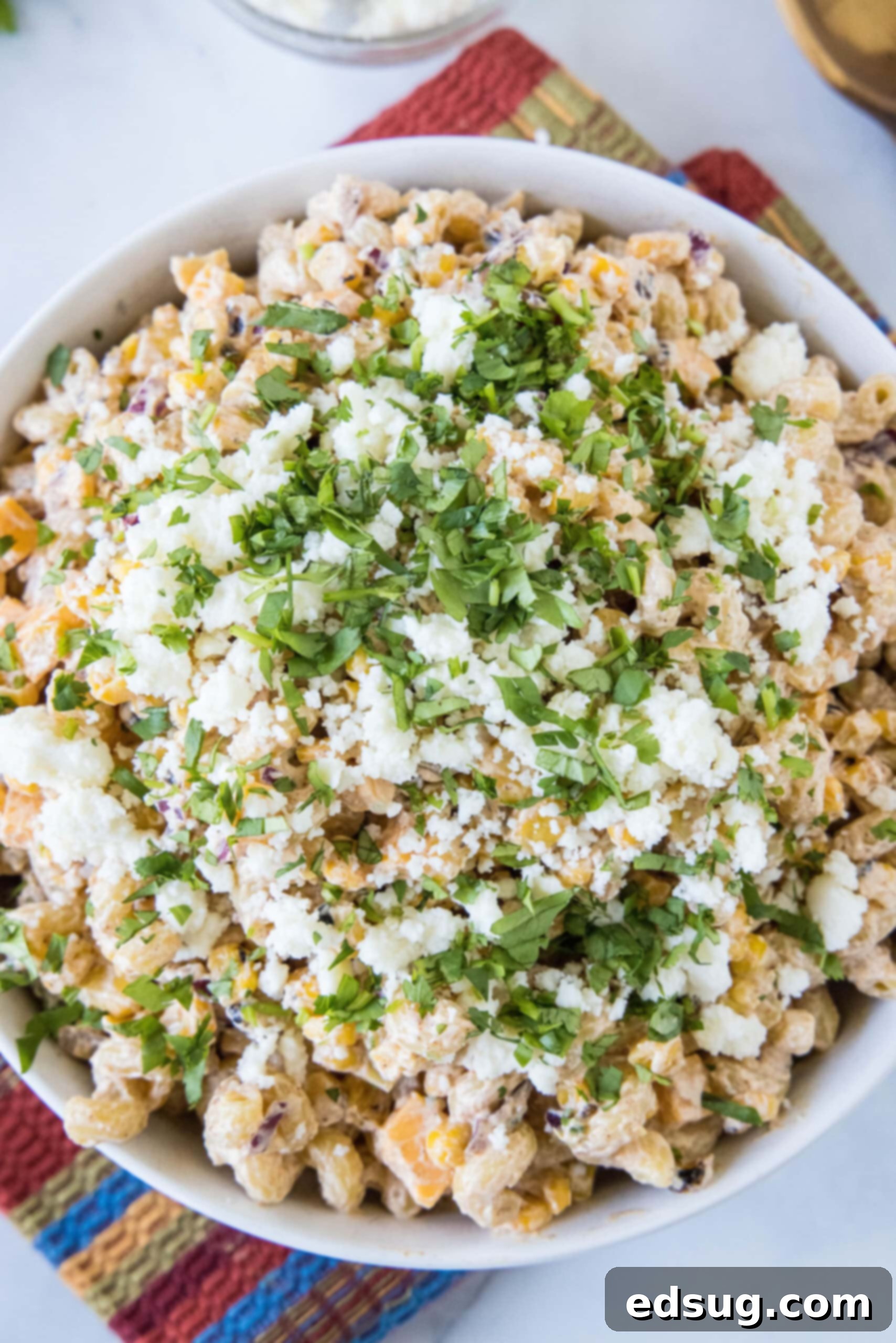An overhead shot of a generous bowl of Mexican street corn pasta salad, artfully garnished with Cotija cheese and fresh cilantro, on a wooden table.