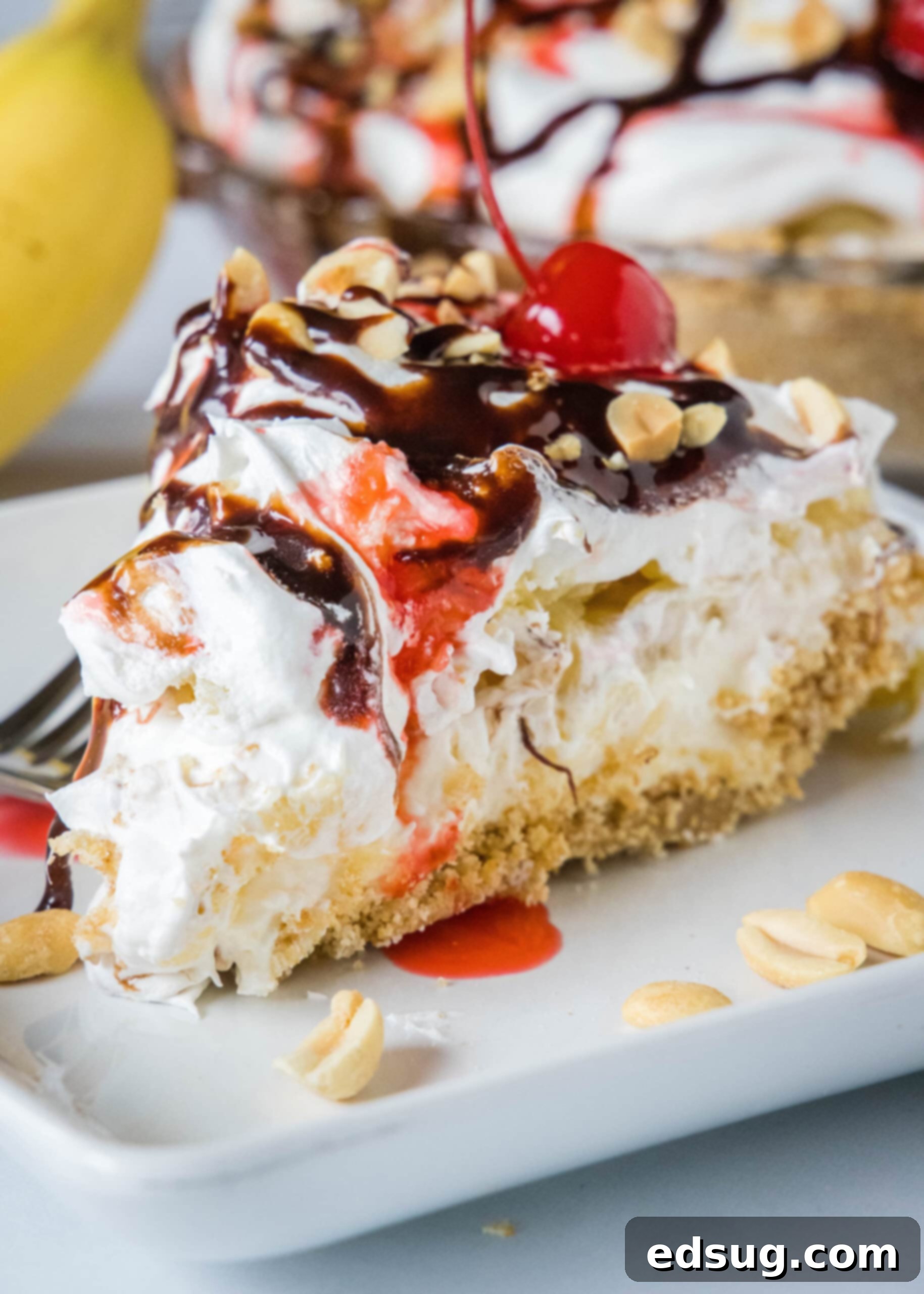 Banana split pie is a cool and creamy no-bake dessert that you can make in 20 minutes. Filled with whipped cream, bananas, and pineapple! A glorious slice of banana split pie, richly drizzled with chocolate and strawberry sauces, adorned with crunchy chopped peanuts and a glistening maraschino cherry, elegantly presented on a plate.