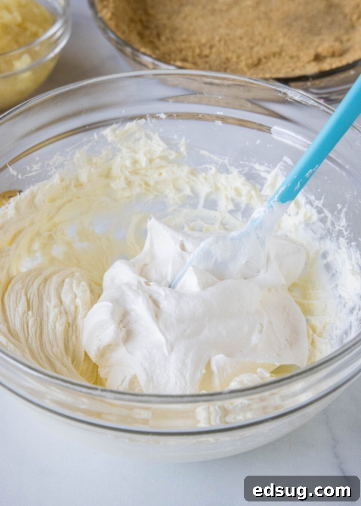 Banana split pie is a cool and creamy no-bake dessert that you can make in 20 minutes. Filled with whipped cream, bananas, and pineapple! Fluffy whipped topping being gently folded into a creamy cream cheese filling in a mixing bowl, ready for the pie.