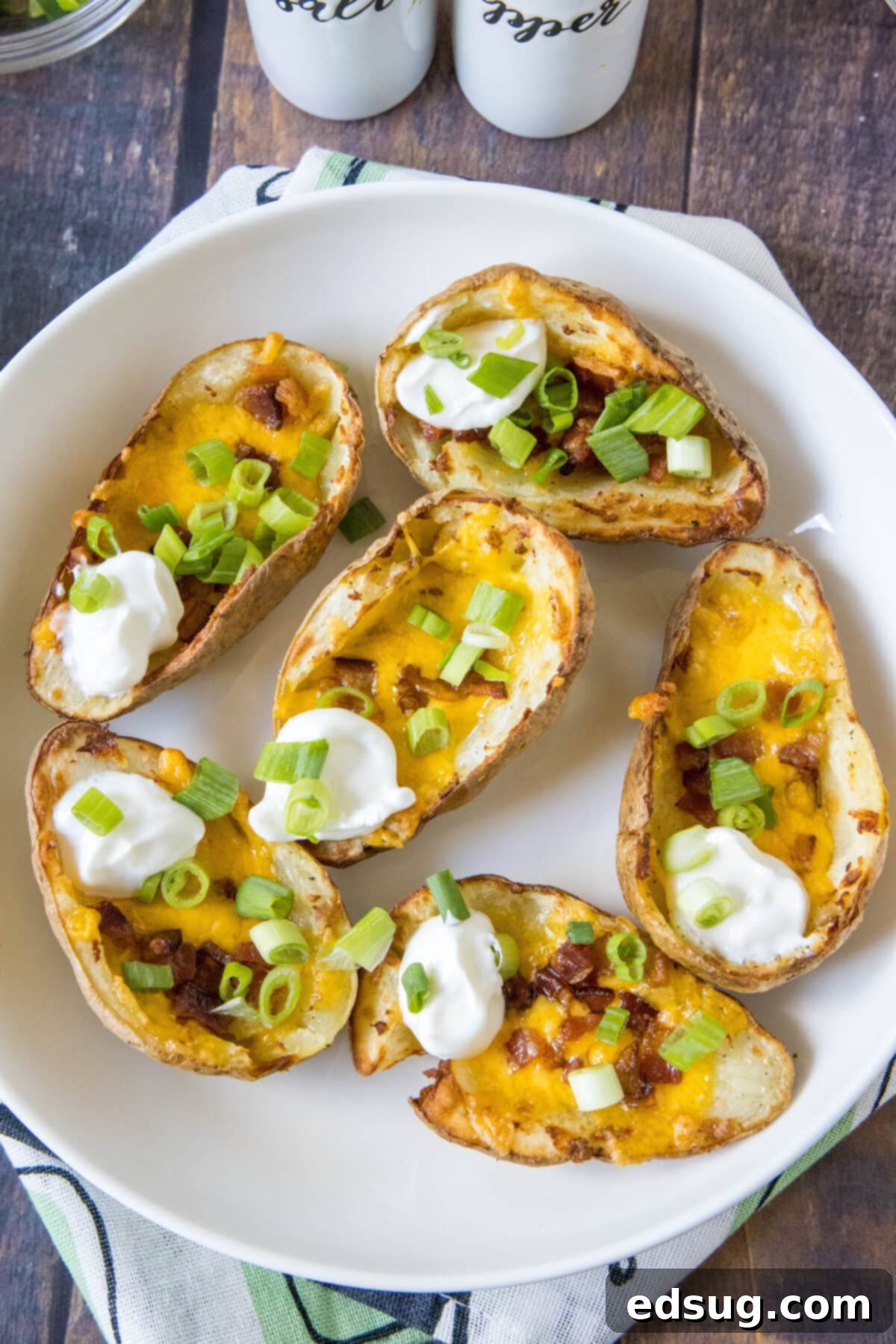 potato skins topped with green onions and sour cream on a serving platter