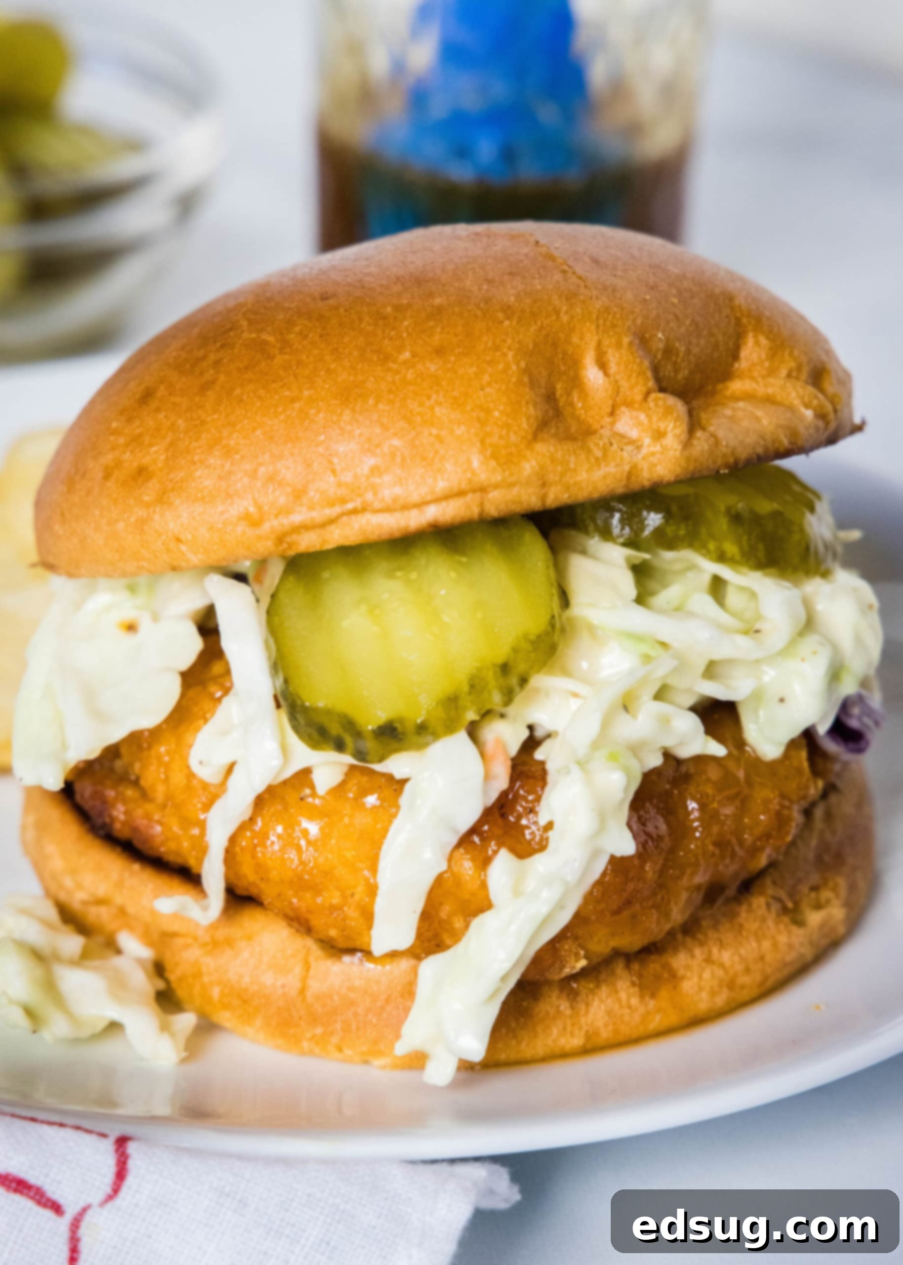 Make a hot honey chicken sandwich with crispy chicken coated in spicy honey, served between fluffy burger buns with cool and crunchy coleslaw! A hot honey chicken sandwich topped with coleslaw and pickles on a white plate.