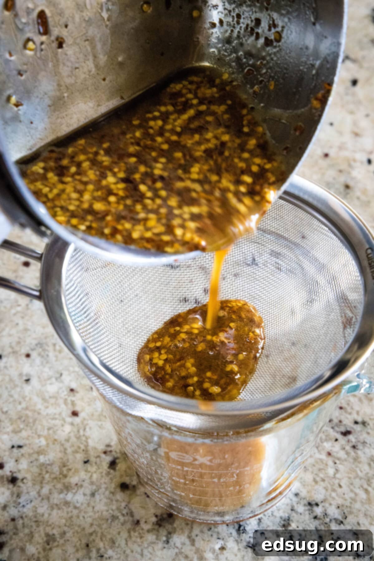 Make a hot honey chicken sandwich with crispy chicken coated with spicy honey, served between fluffy burger buns with cool and crunchy coleslaw! Hot honey being strained into a jar through a mesh sieve.