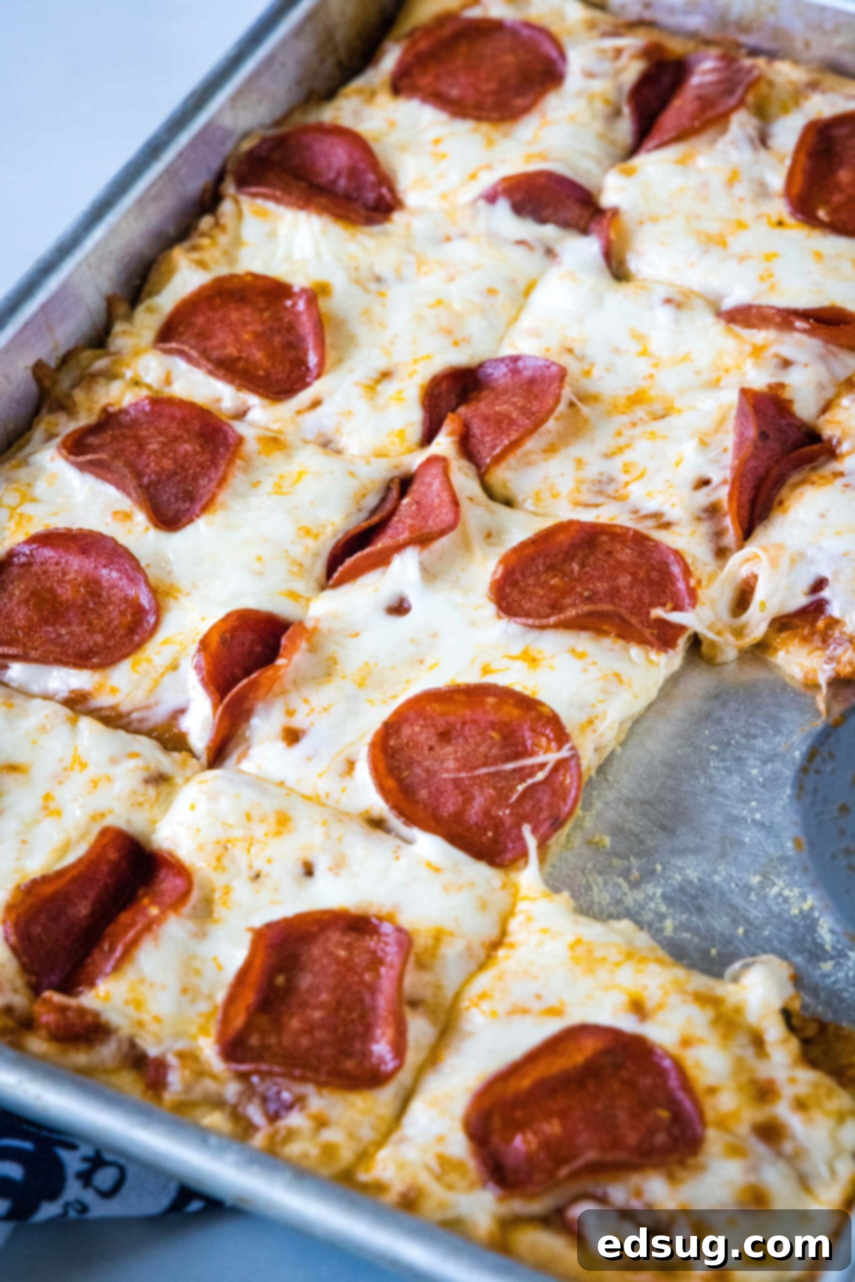 Cheesy crescent roll pizza is the perfect dinner or party snack! There’s zero kneading or rise time, just add your favorite toppings and bake! Pepperoni crescent roll pizza cut into squares on a baking sheet, with one slice missing.