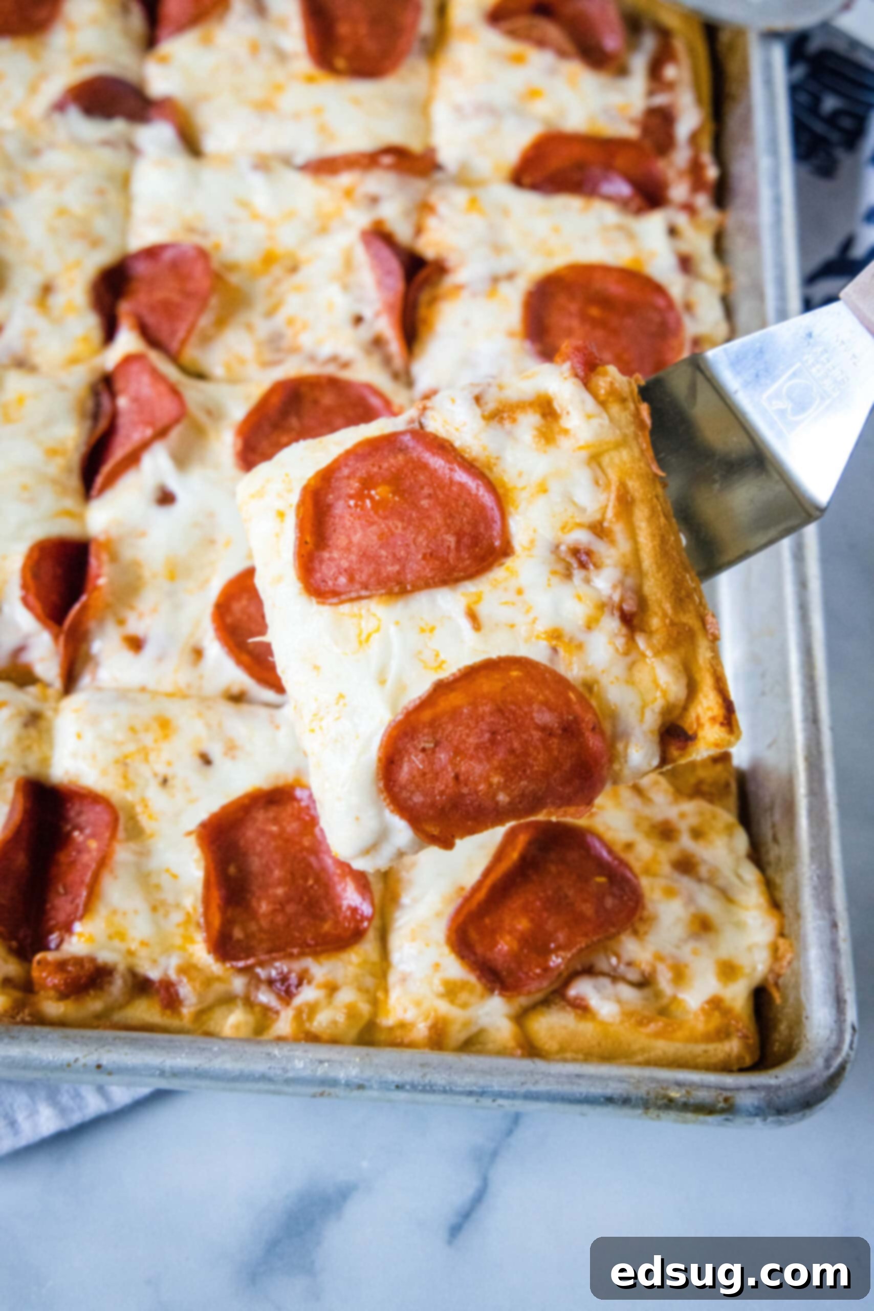 Cheesy crescent roll pizza is the perfect dinner or party snack! There’s zero kneading or rise time, just add your favorite toppings and bake! A spatula holding a pepperoni pizza slice over the rest of the crescent roll pizza on a baking sheet.