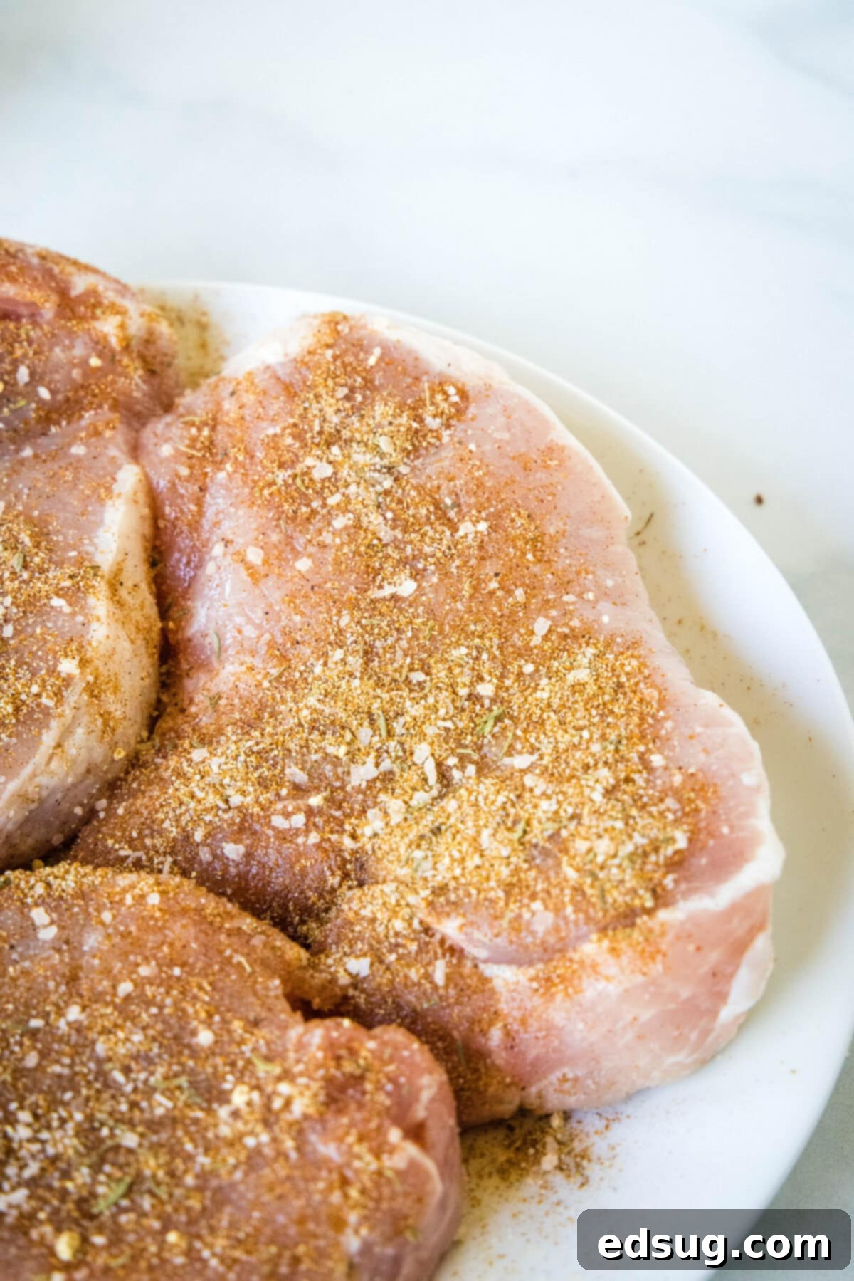 Instant Pot pork chops are perfectly seasoned, perfectly cooked, and so juicy! Pair these easy pork chops with a side of veggies or salad. Seasoned pork chops on a white plate, ready for searing.