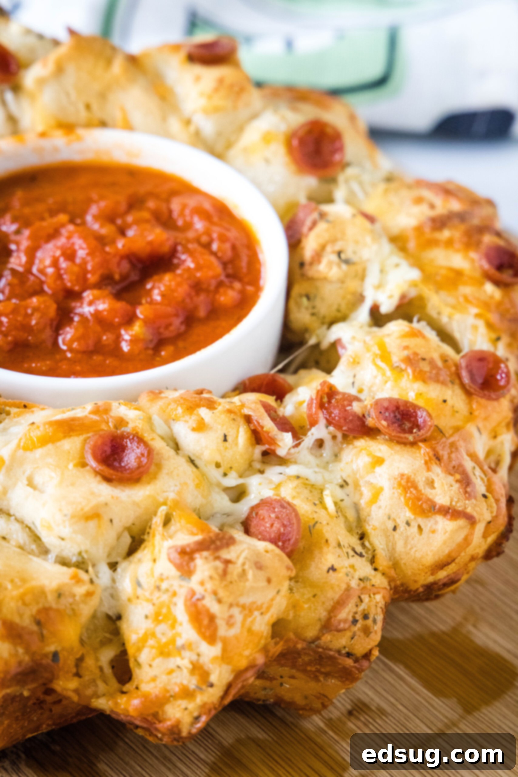 Pizza monkey bread is an easy, pull-apart-style appetizer or dinner made from puffy biscuits baked with pepperoni and lots of melty cheese! Golden brown Pizza Monkey Bread with a small bowl of marinara sauce in the center hole, ready for dipping.