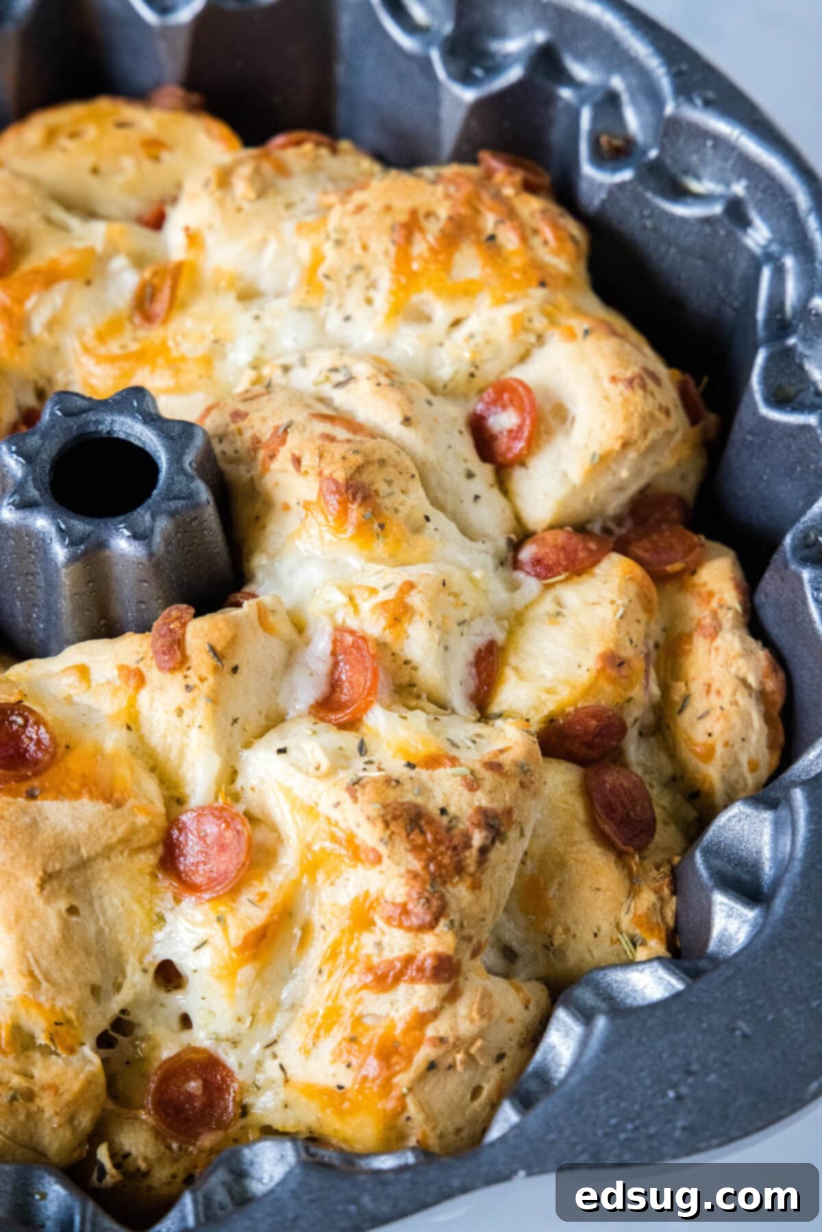 Pizza monkey bread is an easy, pull-apart-style appetizer or dinner made from puffy biscuits baked with pepperoni and lots of melty cheese! A close-up view of baked pizza monkey bread still in the bundt pan, showing its golden-brown, puffed-up texture.