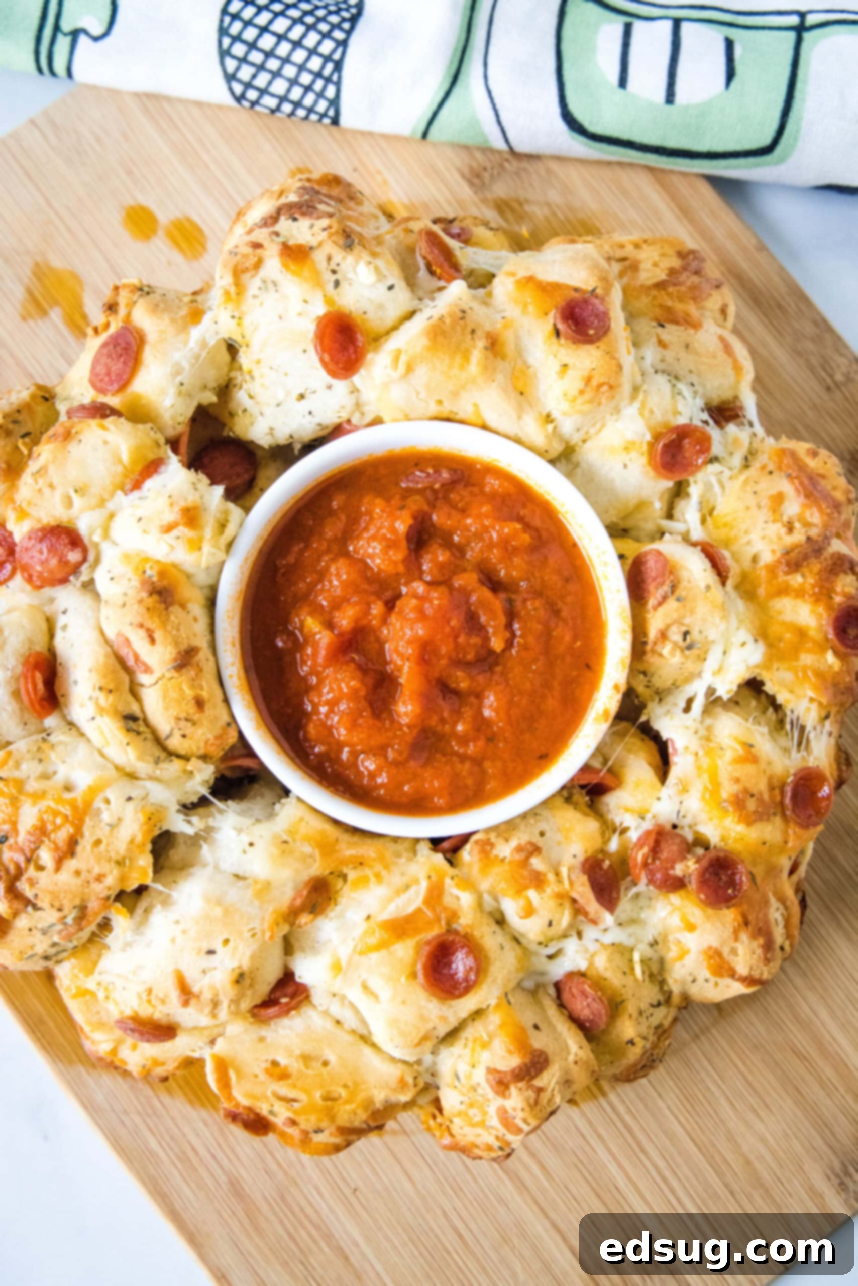 Pizza monkey bread is an easy, pull-apart-style appetizer or dinner made from puffy biscuits baked with pepperoni and lots of melty cheese! An overhead shot of baked Pizza Monkey Bread, showcasing its appealing golden crust and a small bowl of pizza sauce nestled in the center.