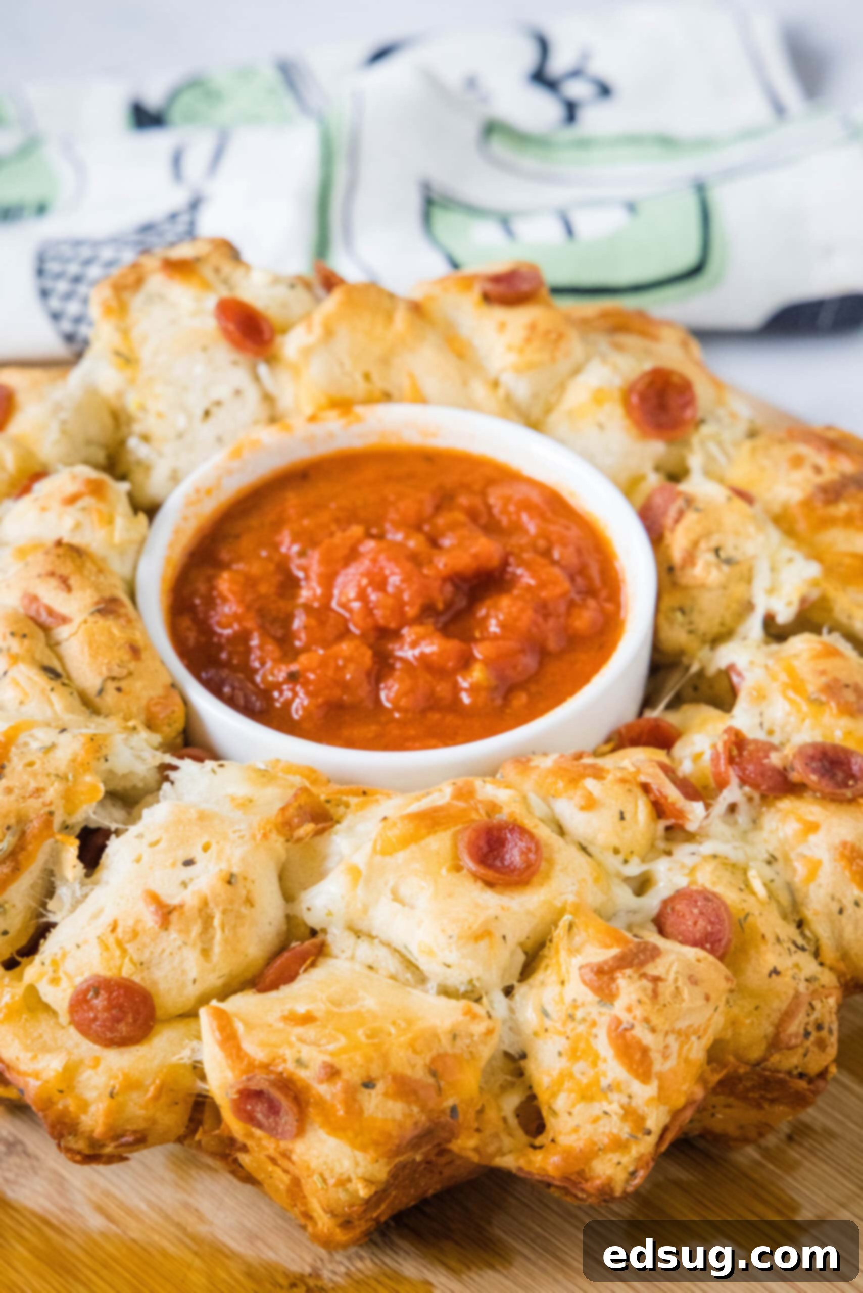 Pizza monkey bread is an easy, pull-apart-style appetizer or dinner made from puffy biscuits baked with pepperoni and lots of melty cheese! A complete Pizza Monkey Bread presentation with a dipping bowl in the center, ready to be enjoyed as a meal or appetizer.