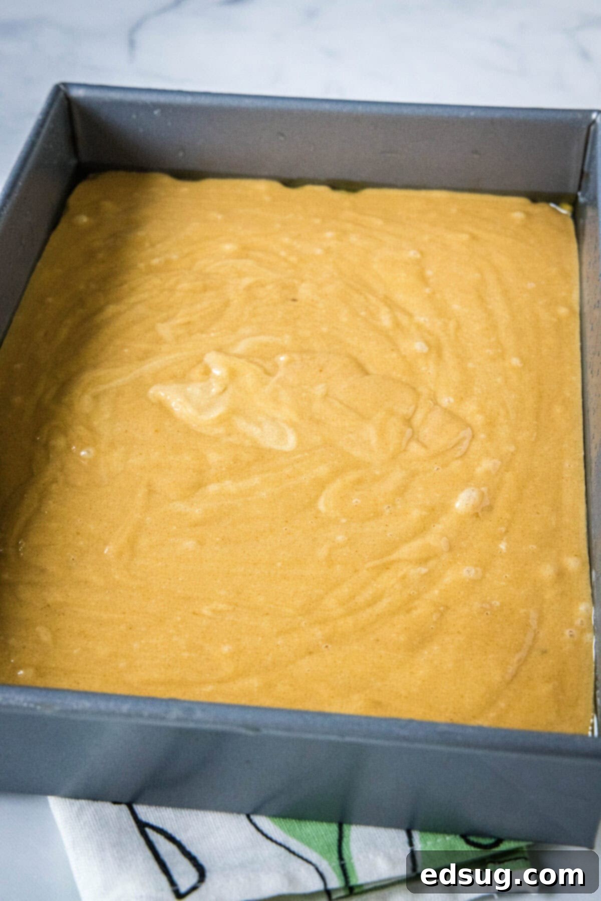 Smooth peanut butter cake batter poured evenly into a 9x13 inch sheet pan, ready for baking.