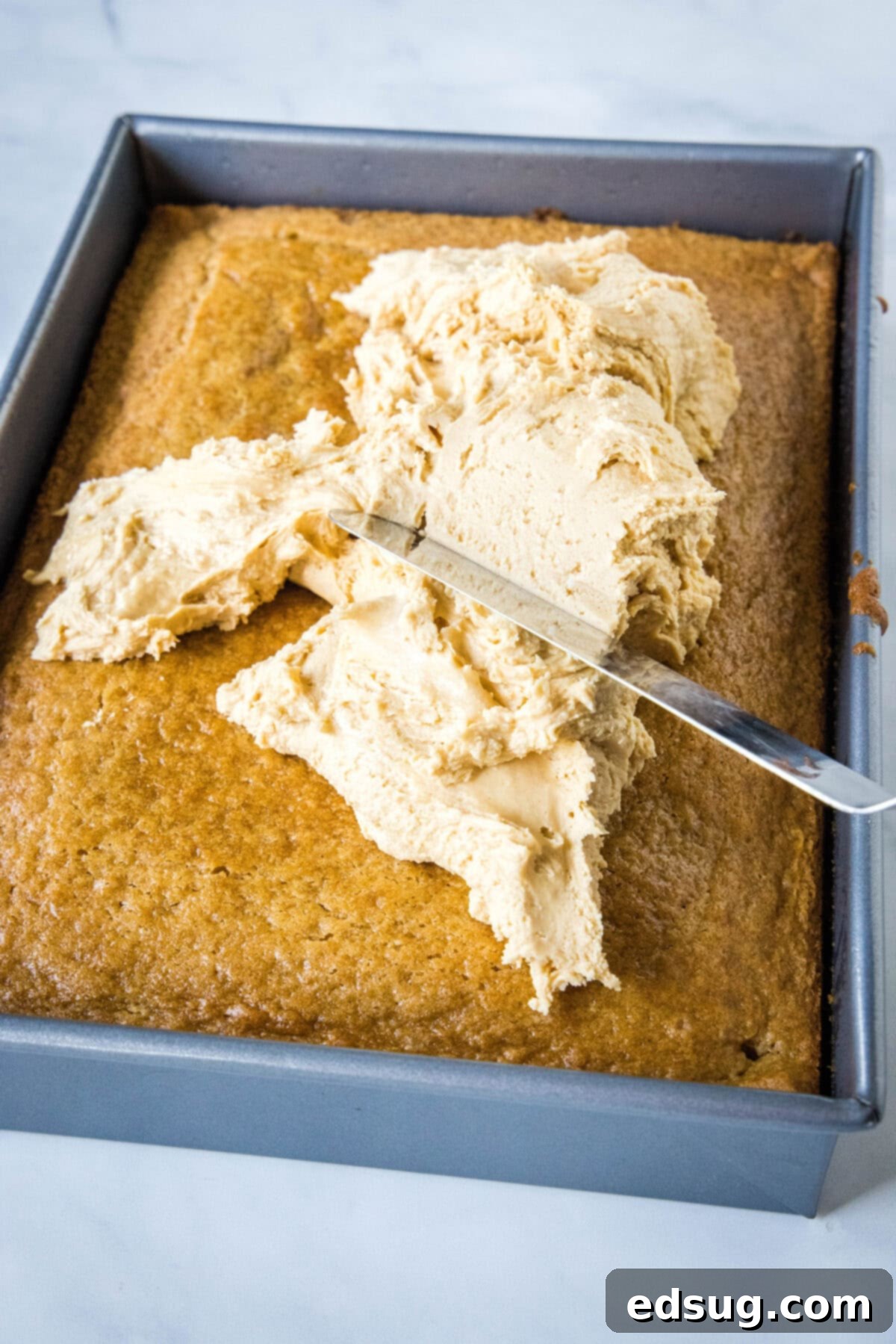 Deliciously creamy peanut butter frosting being expertly spread over a cooled peanut butter cake in a sheet pan, creating a smooth, even layer.