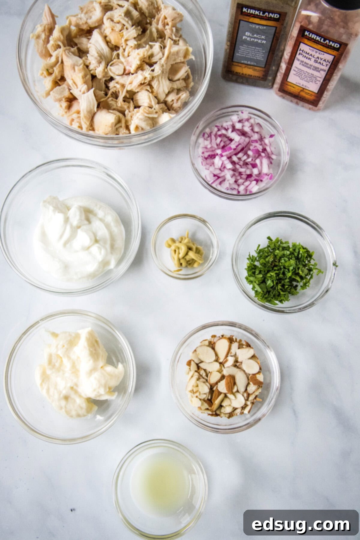Fresh ingredients for healthy chicken salad laid out: shredded chicken, Greek yogurt, red onion, lemon, dijon, parsley, and almonds.