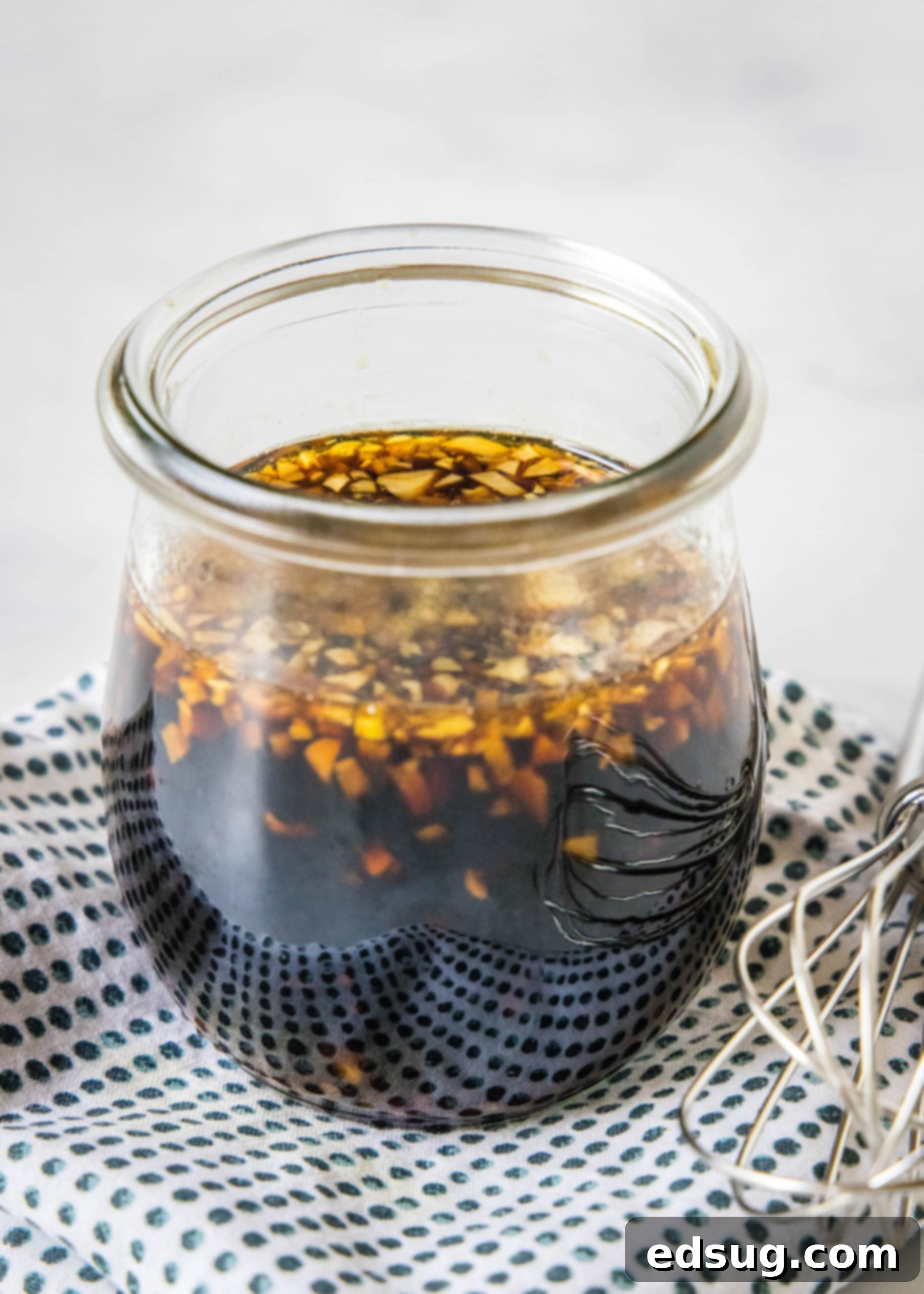 Homemade teriyaki sauce in a glass jar on a blue and white polka dot napkin, next to a whisk.