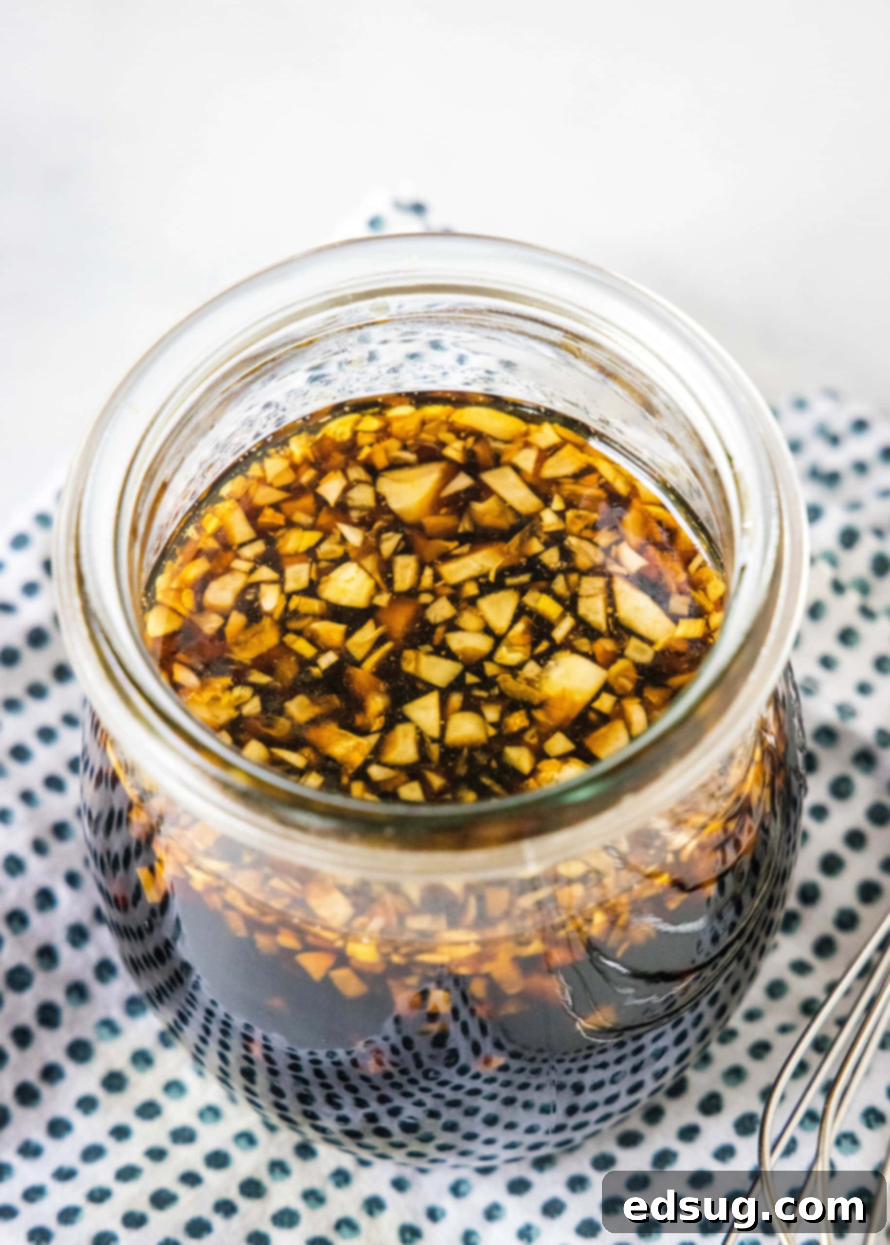 Close up of homemade teriyaki sauce in a glass jar on a blue and white polka dot napkin.