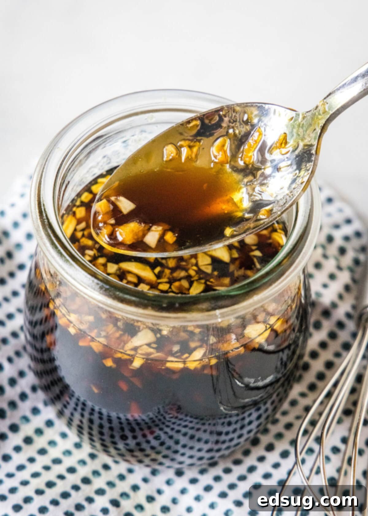 A spoon drizzling teriyaki sauce into a glass jar.