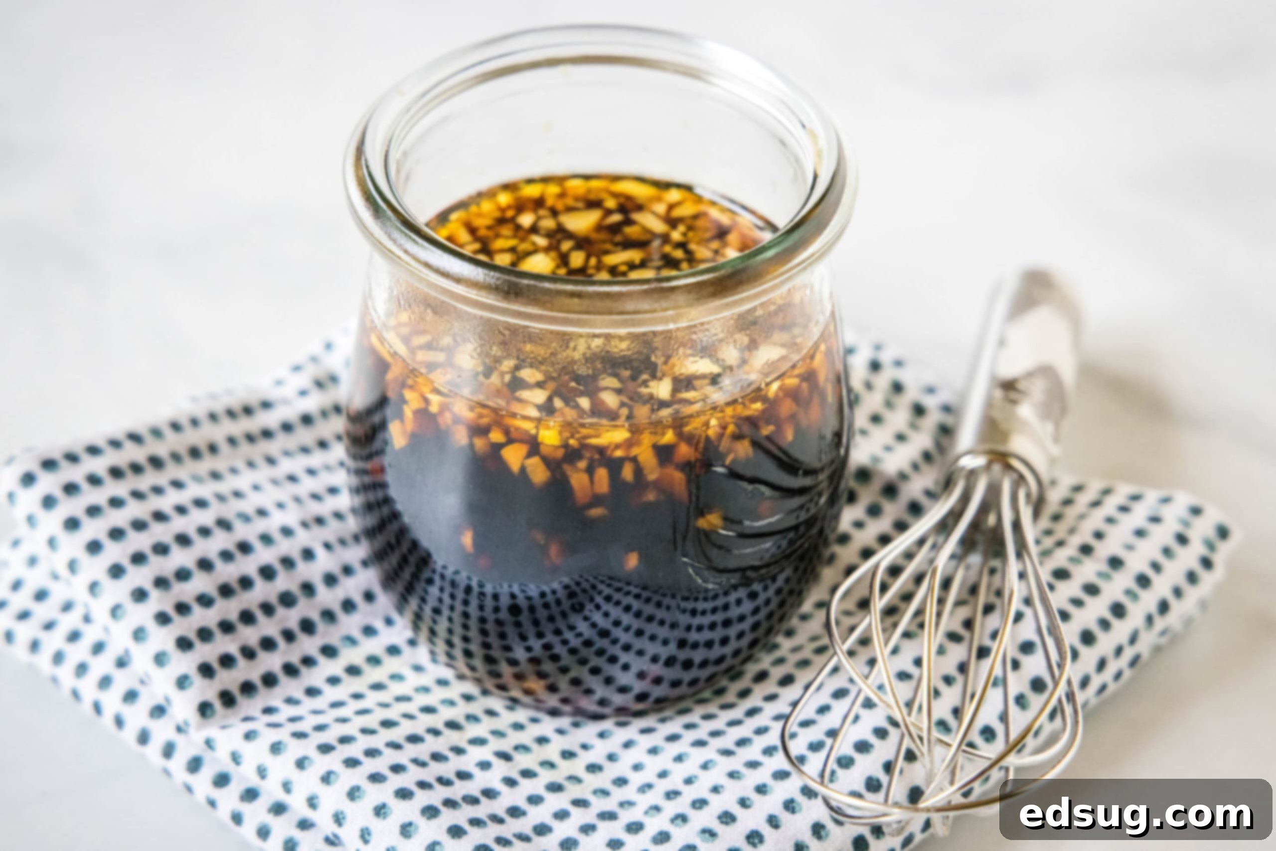 Homemade teriyaki sauce in a glass jar on a blue and white polka dot napkin, next to a whisk.