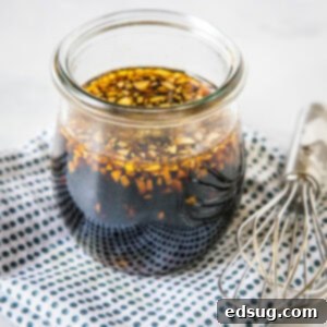 Homemade teriyaki sauce in a glass jar on a blue and white polka dot napkin, next to a whisk.
