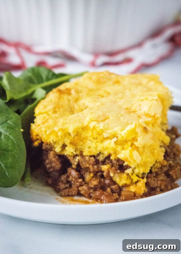 Hearty Sloppy Joe Cornbread Pie 2 A plate with a serving of Sloppy Joe Cornbread Casserole and a side of fresh spinach.