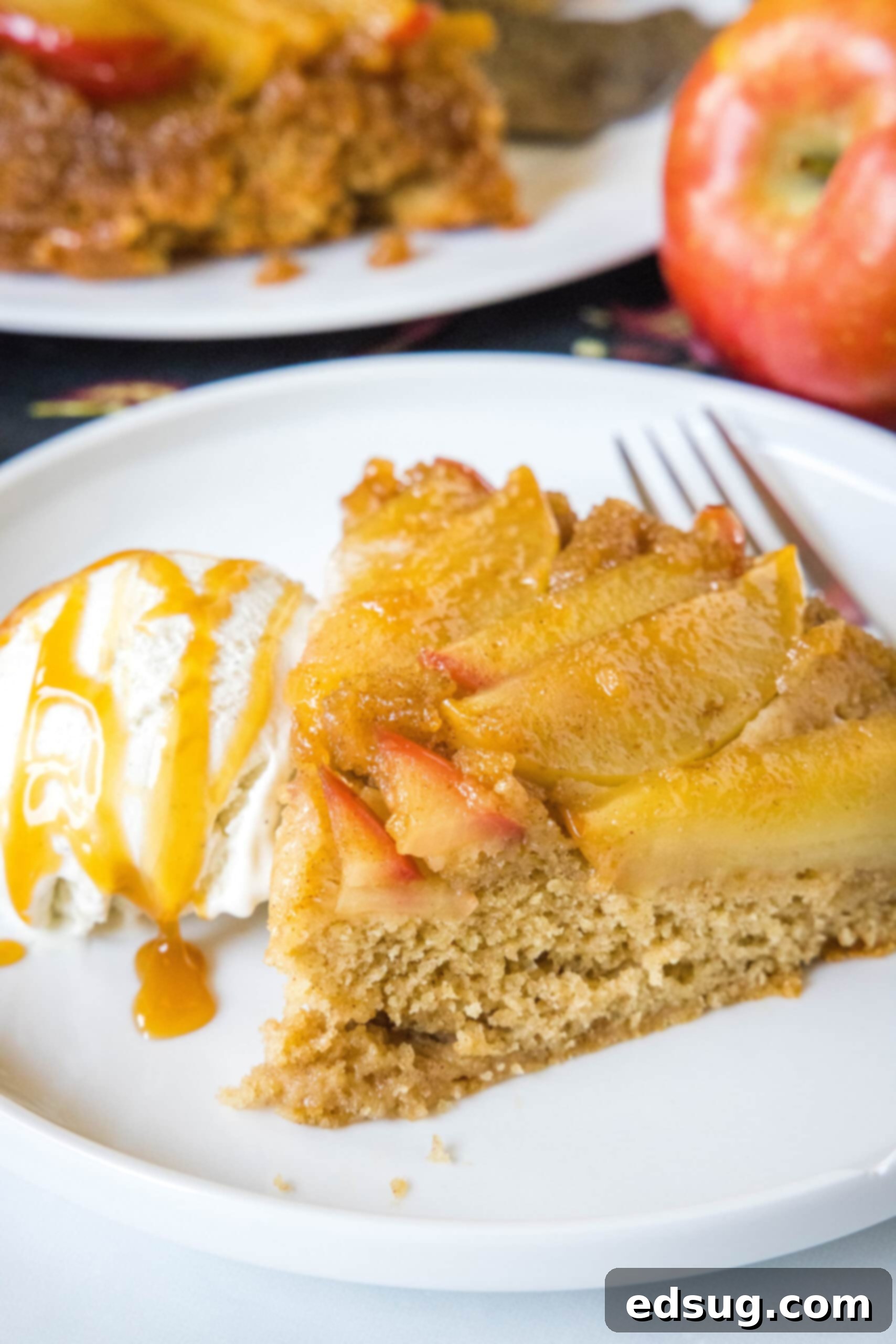 A perfectly baked slice of apple upside down cake served on a pristine white plate, accompanied by a generous scoop of creamy vanilla ice cream drizzled with golden caramel sauce, and a fork ready for indulgence.