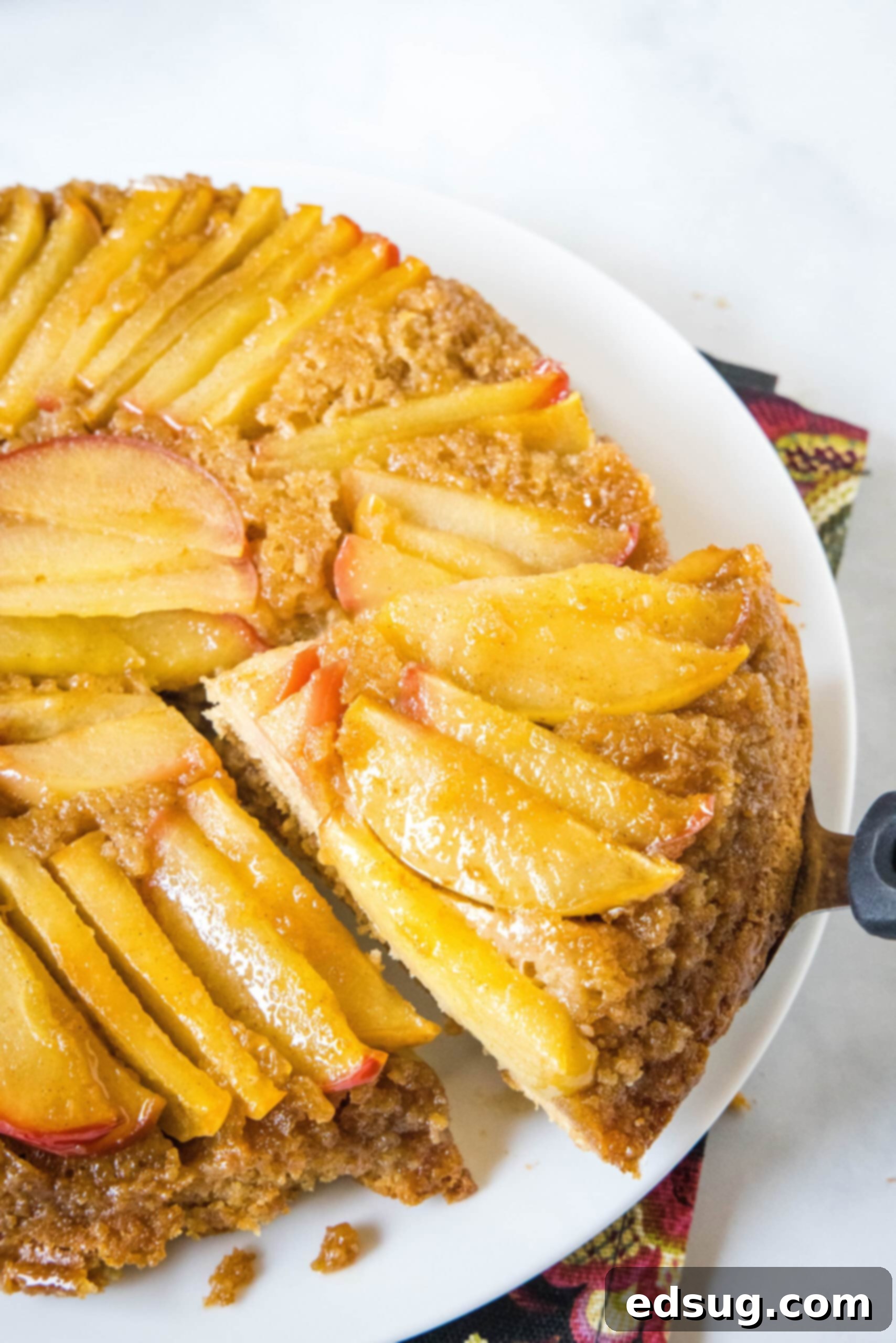 A serving spatula lifting a perfect slice of apple upside down cake from the main cake on a white plate, ready to be enjoyed.