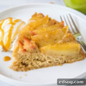 A slice of our delectable apple upside down cake, accompanied by a scoop of melting ice cream and a drizzle of caramel sauce, presented on a white plate with a fork.