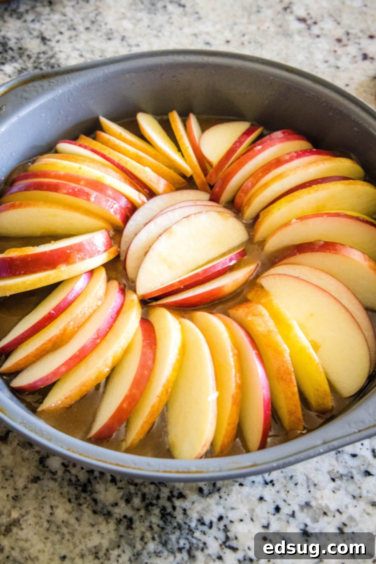 Thinly sliced apples meticulously arranged in a beautiful fan shape over the freshly poured caramel layer at the bottom of a round baking pan, preparing for an apple upside down cake.