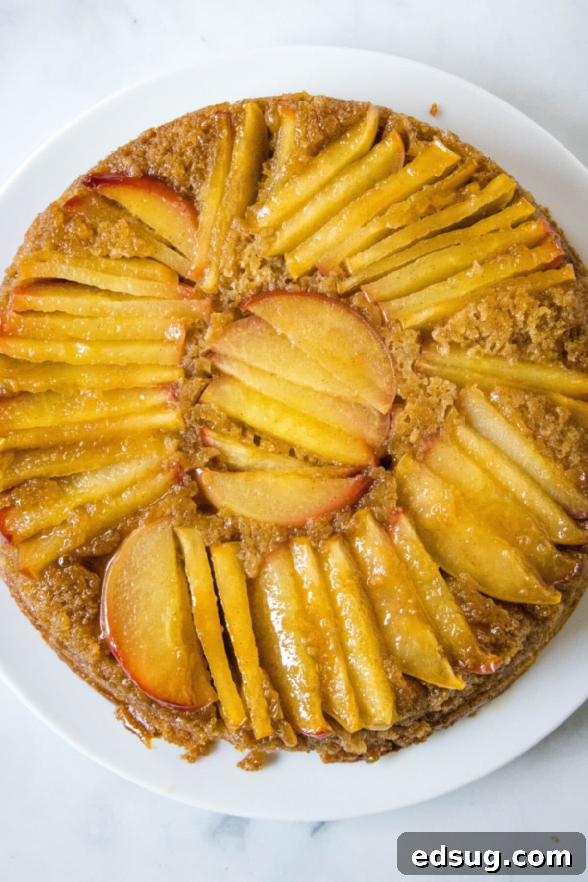 An inviting overhead view of a beautifully golden apple upside down cake, perfectly inverted and presented on a white serving plate, ready to be sliced and enjoyed.