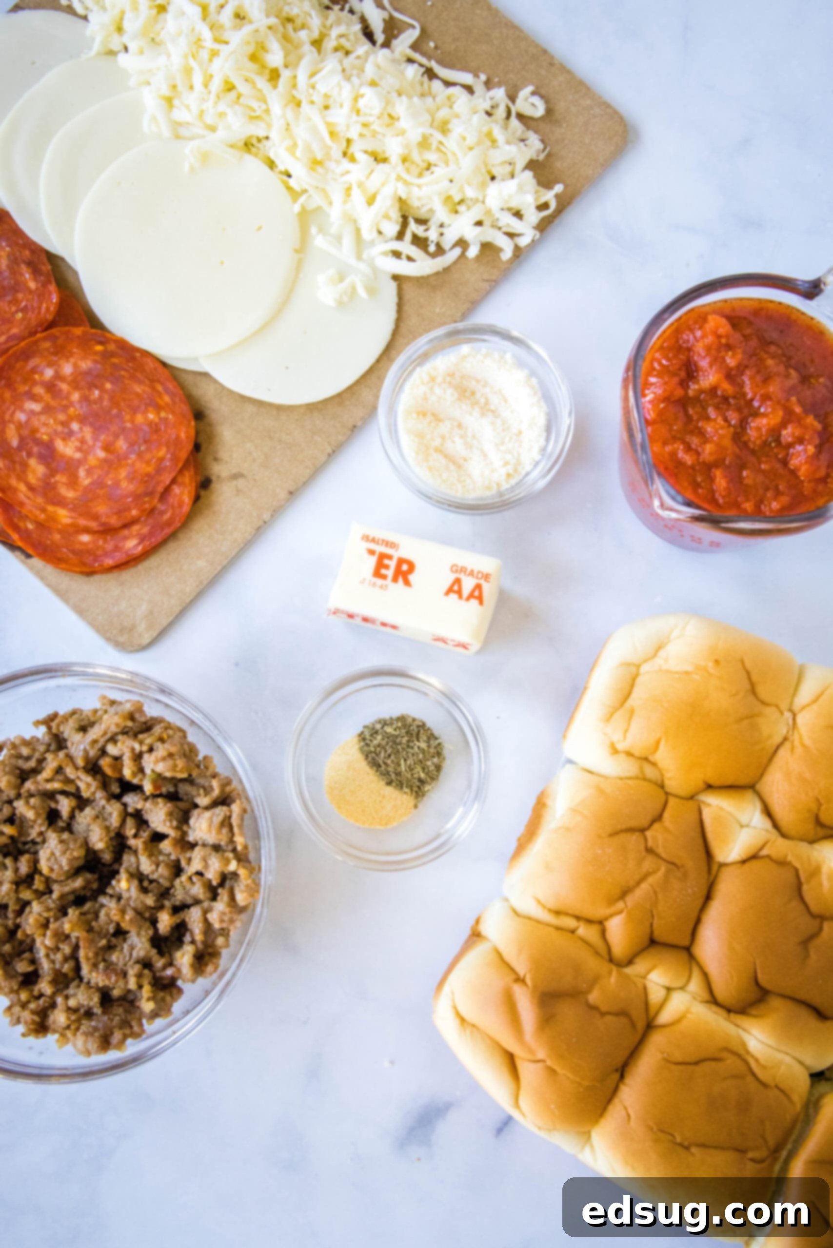 Hawaiian roll pizza sliders are a fun appetizer or weeknight family dinner! They're quick and easy to make with your favorite pizza toppings. A beautiful flat lay of all the essential ingredients needed for Hawaiian roll pizza sliders, neatly arranged on a rustic wooden board. Included are a pack of Hawaiian rolls, a jar of pizza sauce, blocks and slices of various cheeses like provolone and cheddar, a packet of sliced pepperoni, crumbled cooked Italian sausage, and small bowls of melted butter with seasonings for the garlic butter topping.