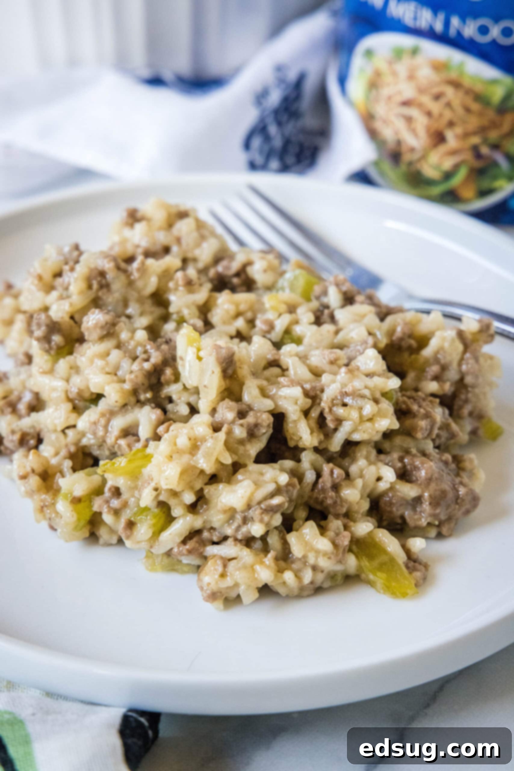 Hamburger rice casserole is an easy retro dinner recipe with fluffy rice, juicy ground beef, and veggies cooked in cream of mushroom soup! A serving of hamburger rice casserole next to a fork on a white plate.