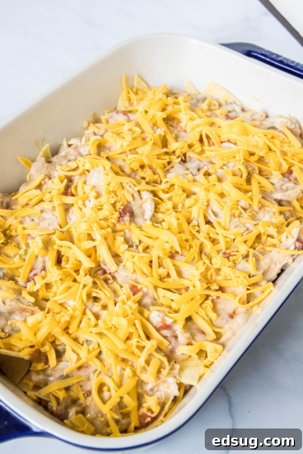 Unbaked King Ranch chicken casserole topped with a generous layer of shredded cheese in a baking dish, ready for the oven.
