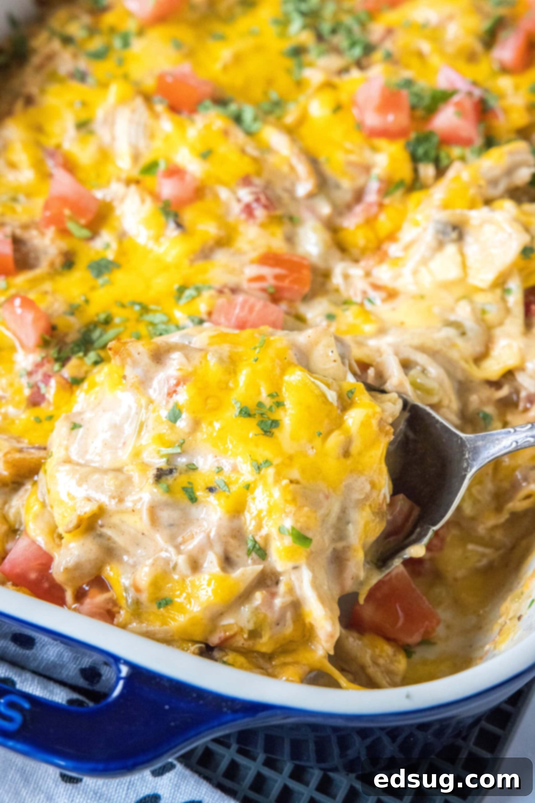 A spoon scooping a generous serving of hot, cheesy King Ranch chicken casserole from a baking dish.