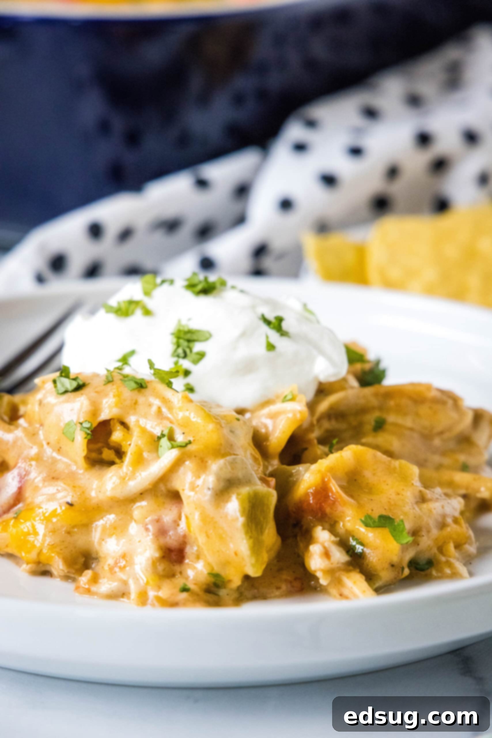 A serving of King Ranch chicken casserole topped with a dollop of sour cream on a white plate next to a fork, ready to be enjoyed.