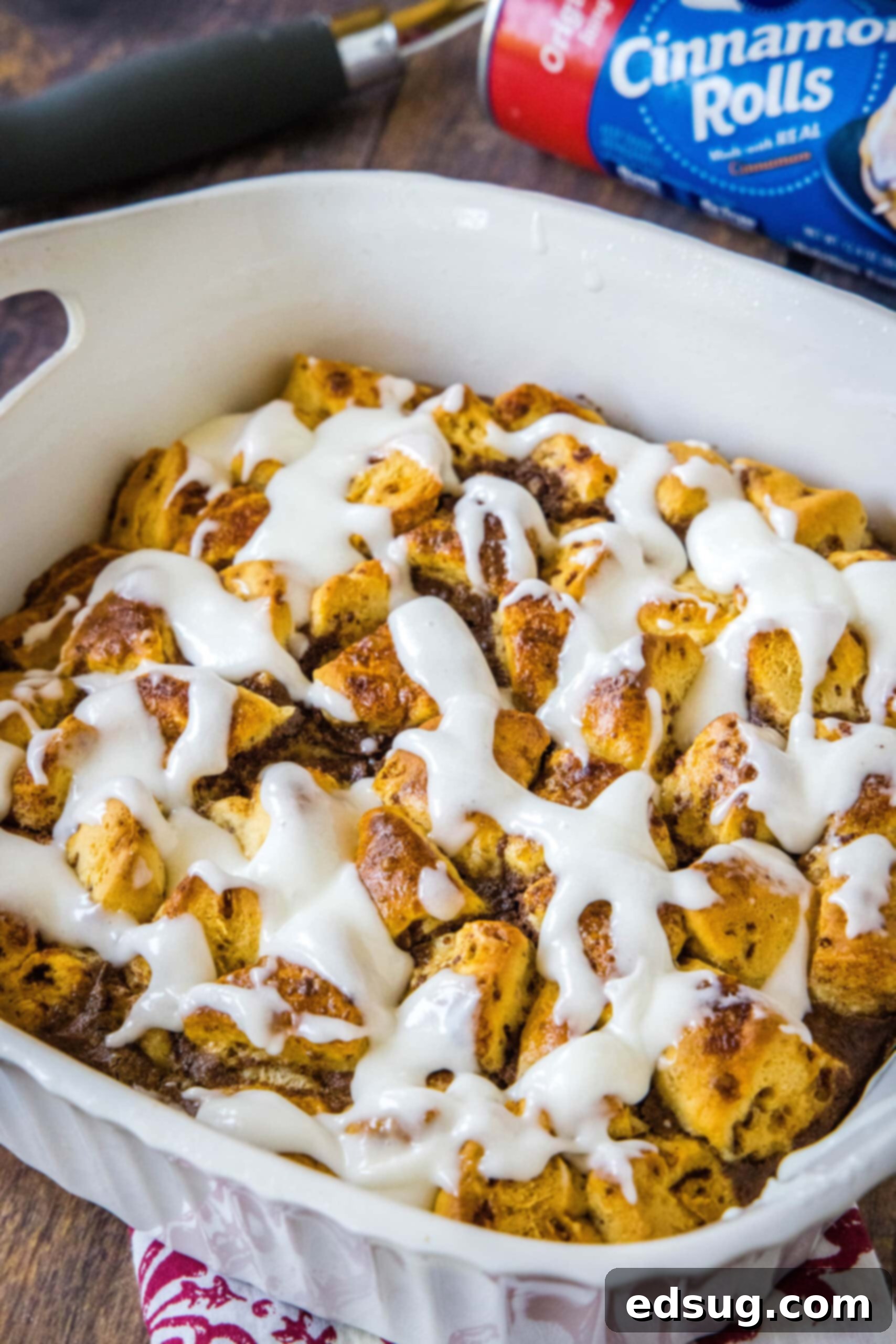 Cinnamon roll casserole is a quick and easy breakfast casserole with flaky layers baked in a rich and creamy custard. Perfect for a crowd! A freshly baked cinnamon roll casserole in a ceramic baking dish, beautifully drizzled with white icing, showcasing its golden-brown crust and inviting texture.