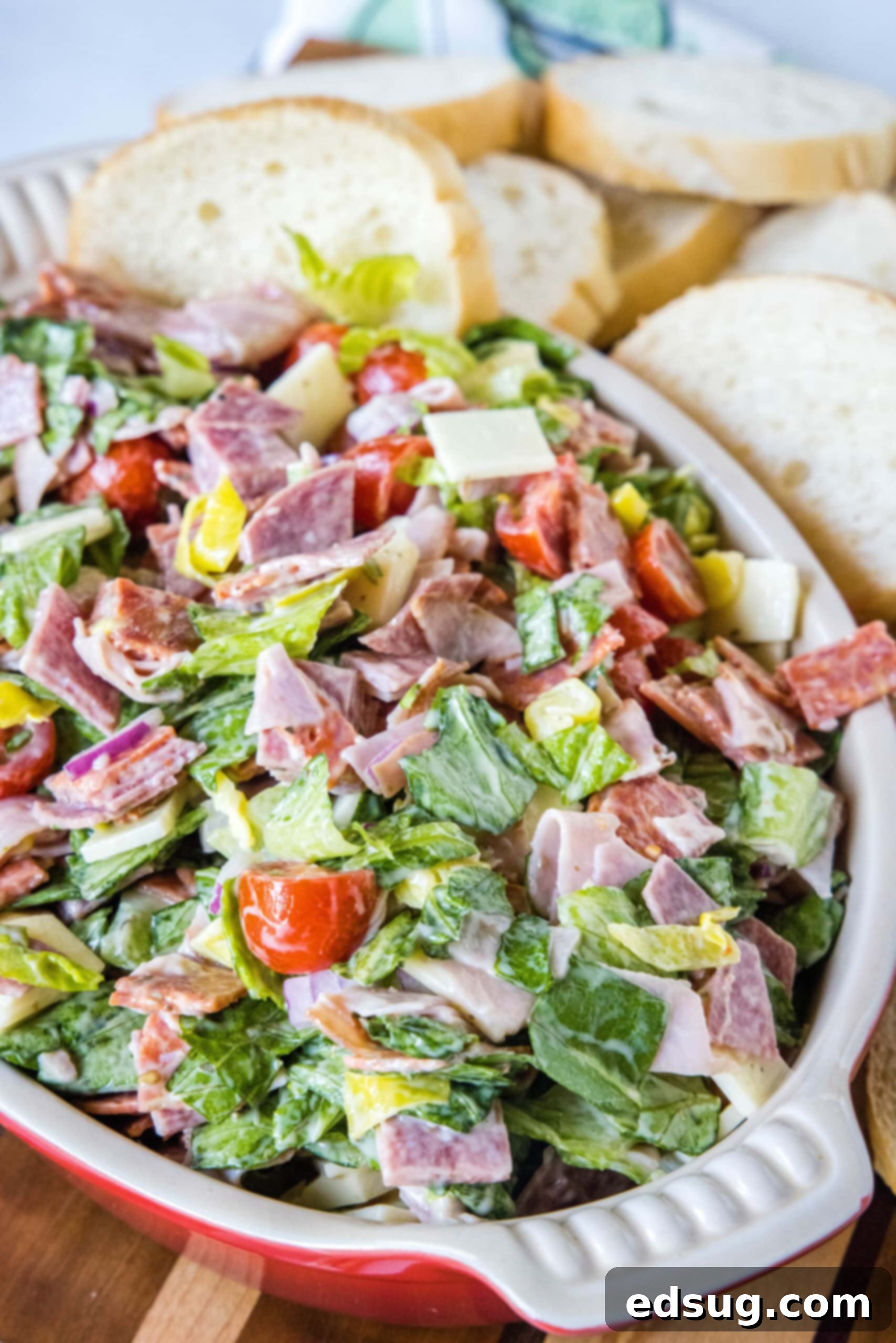 This fresh and zesty hoagie dip has all the flavors of an Italian sub sandwich! Serve this dip as an easy appetizer spread over crusty bread. Hoagie dip in a red ceramic serving bowl with bread slices in the background.