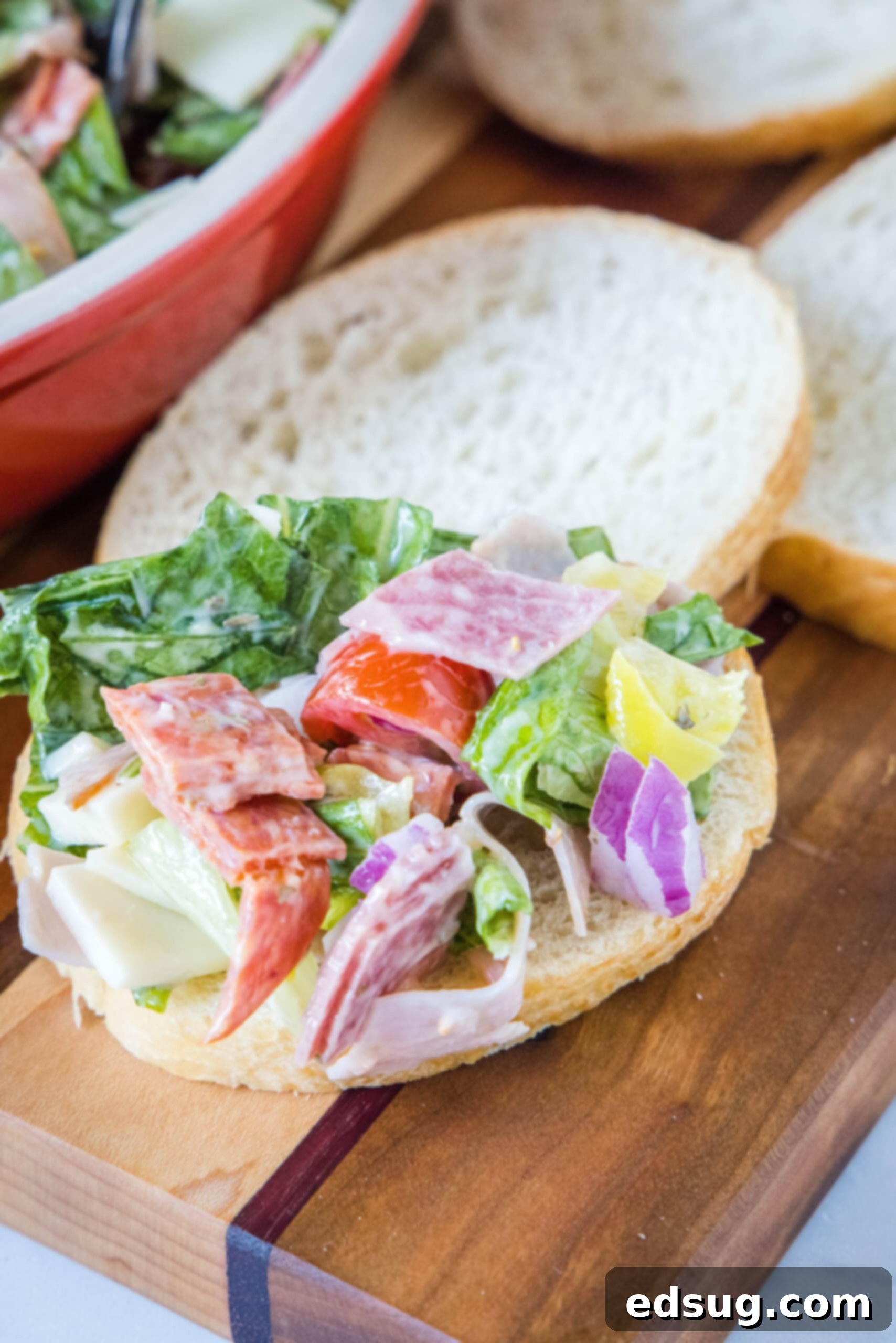 This fresh and zesty hoagie dip has all the flavors of an Italian sub sandwich! Serve this dip as an easy appetizer spread over crusty bread. Hoagie dip piled onto a slice of bread with more bread slices and the bowl of dip in the background.