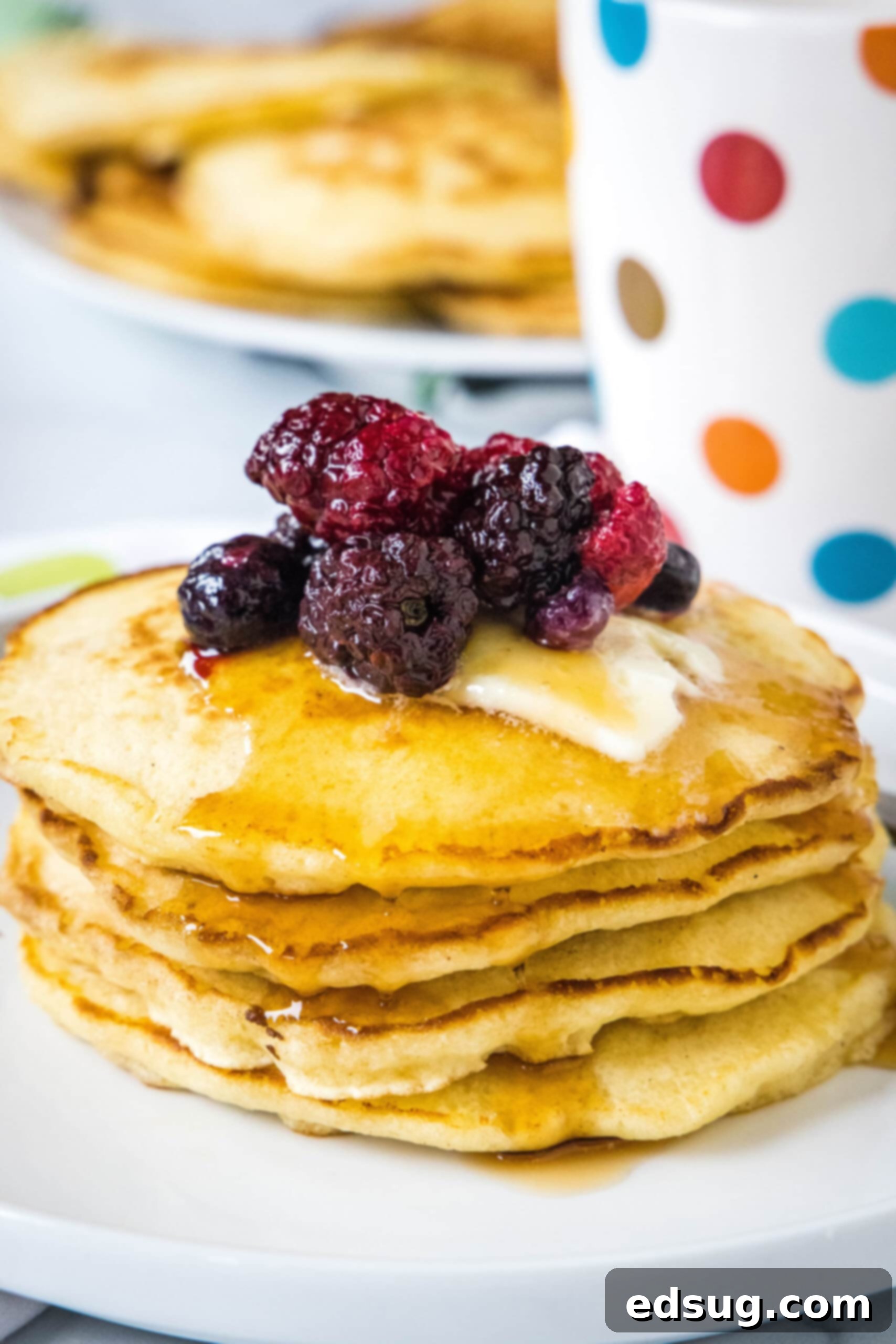 A stack of griddle cakes topped with mixed berries and syrup on a white plate, showcasing their fluffy texture and golden-brown edges.
