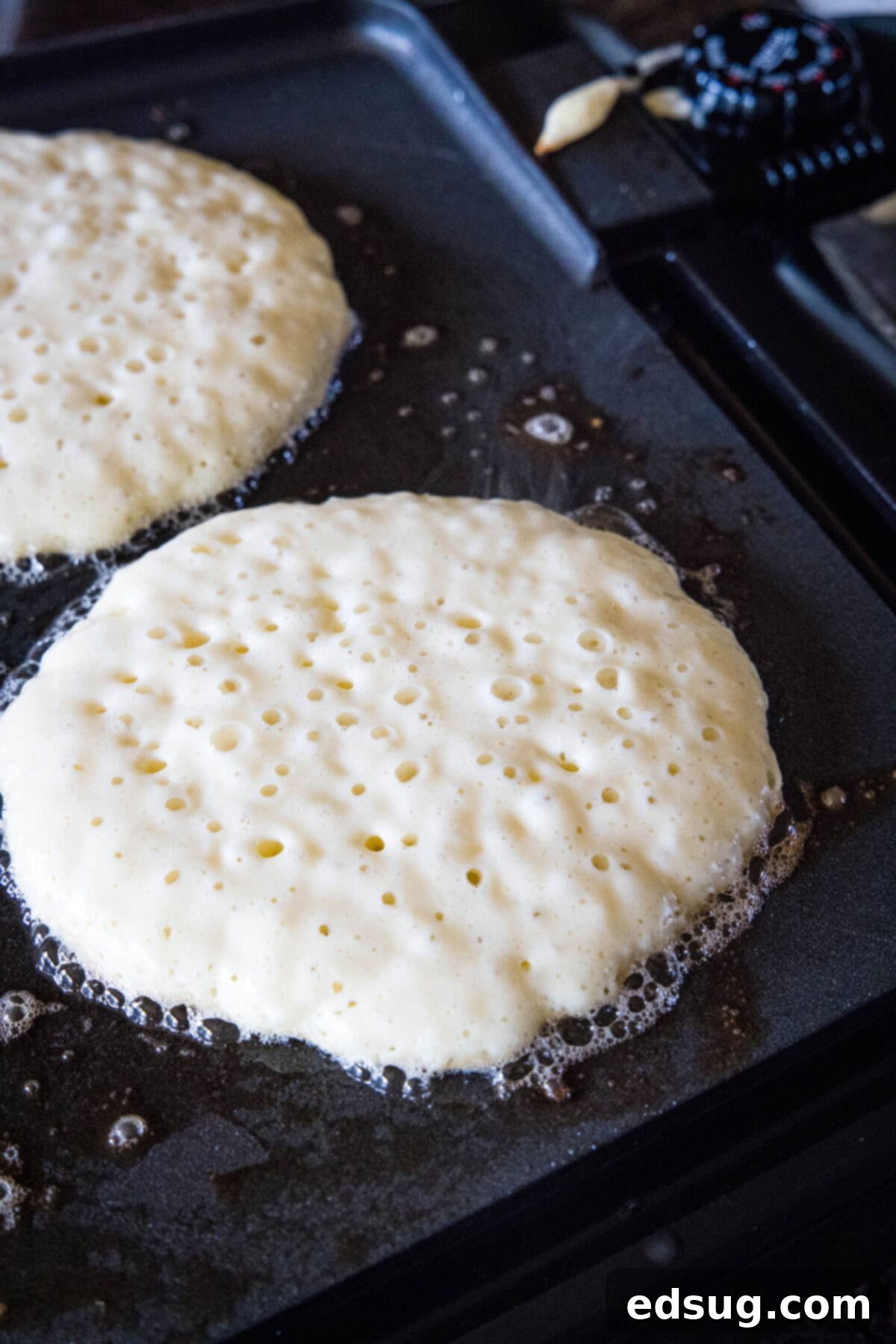 Griddle cake batter cooking on a skillet, with numerous bubbles forming on the surface, indicating it's almost ready to flip.