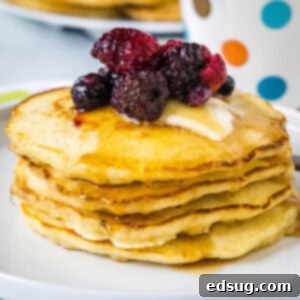 A stack of griddle cakes topped with mixed berries and syrup on a white plate, showcasing fluffy texture and golden edges.