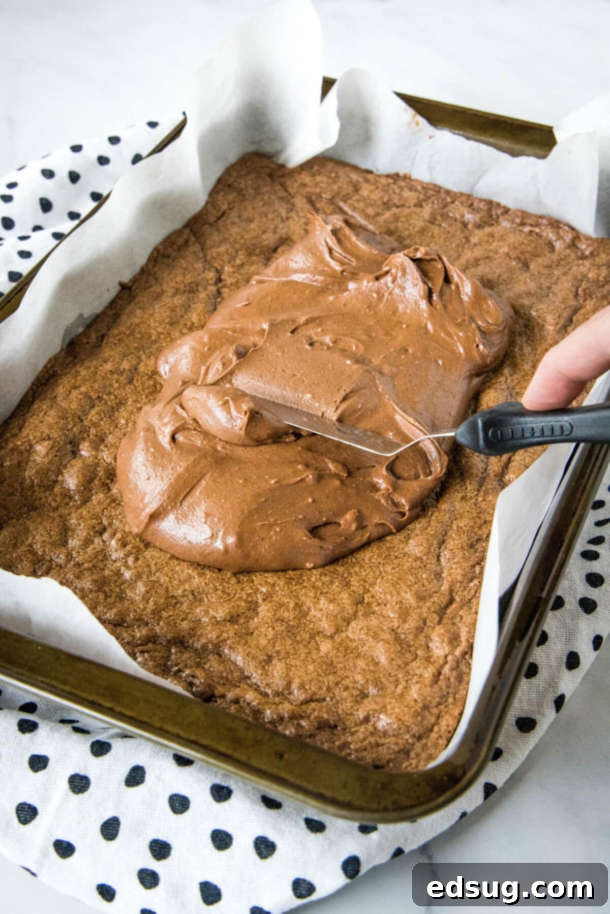 Legendary Lunchroom Brownies 2 Creamy chocolate frosting being smoothly spread over still-warm brownies in a baking pan, creating a glossy top.
