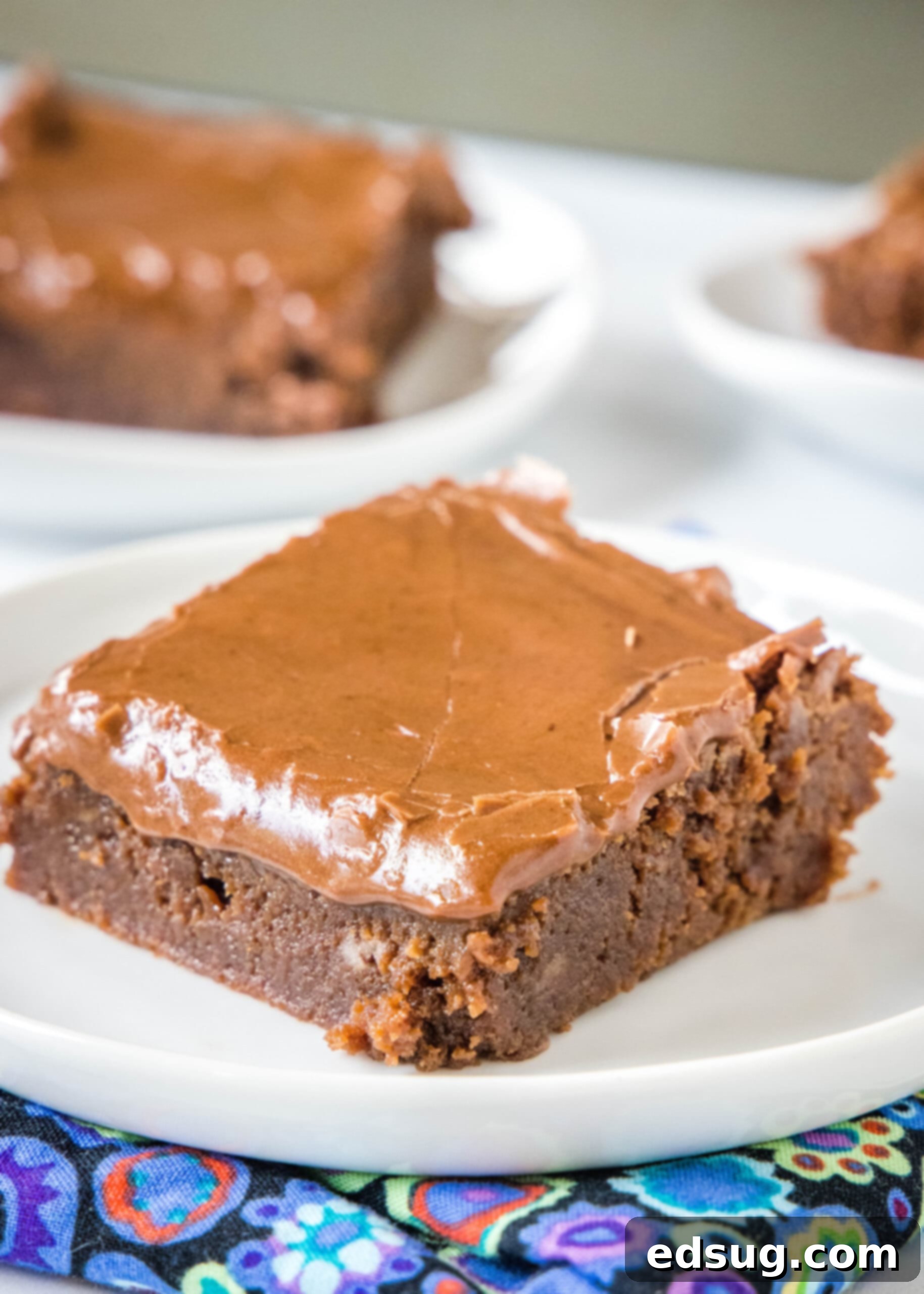Lunch lady brownies are moist, fudgy brownies just like the ones served at school lunches! Every bite is filled with chocolate flavor. A single square of lunch lady brownie on a white plate, with a fork next to it. More brownies are blurred in the background on other plates.